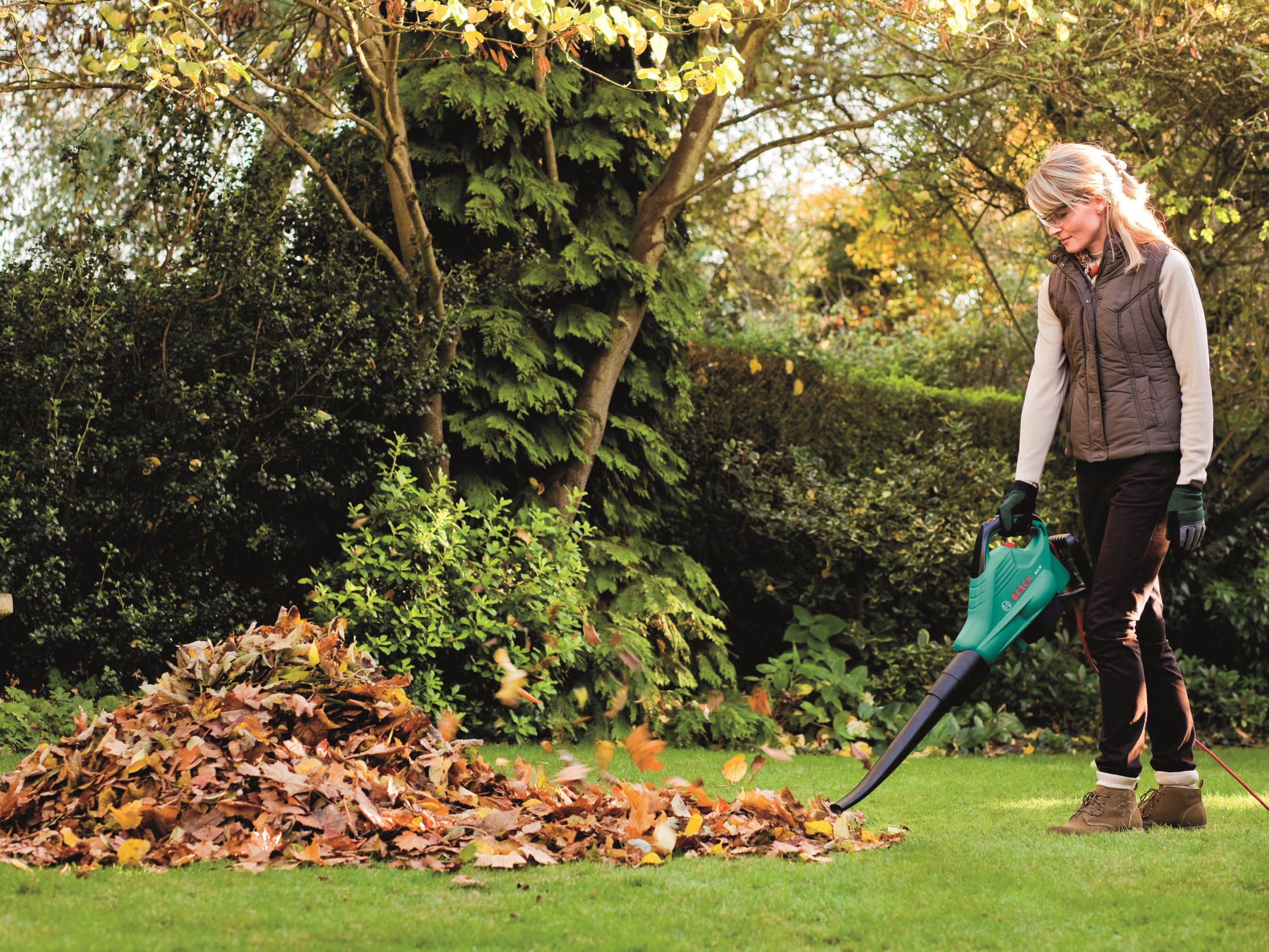 Nő megtisztítja a gyepet az őszi levelektől lombfúvóval