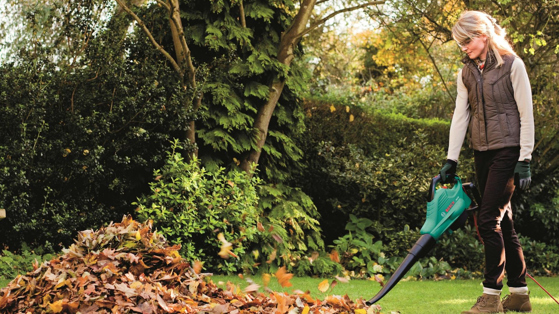 Nő megtisztítja a gyepet az őszi levelektől lombfúvóval