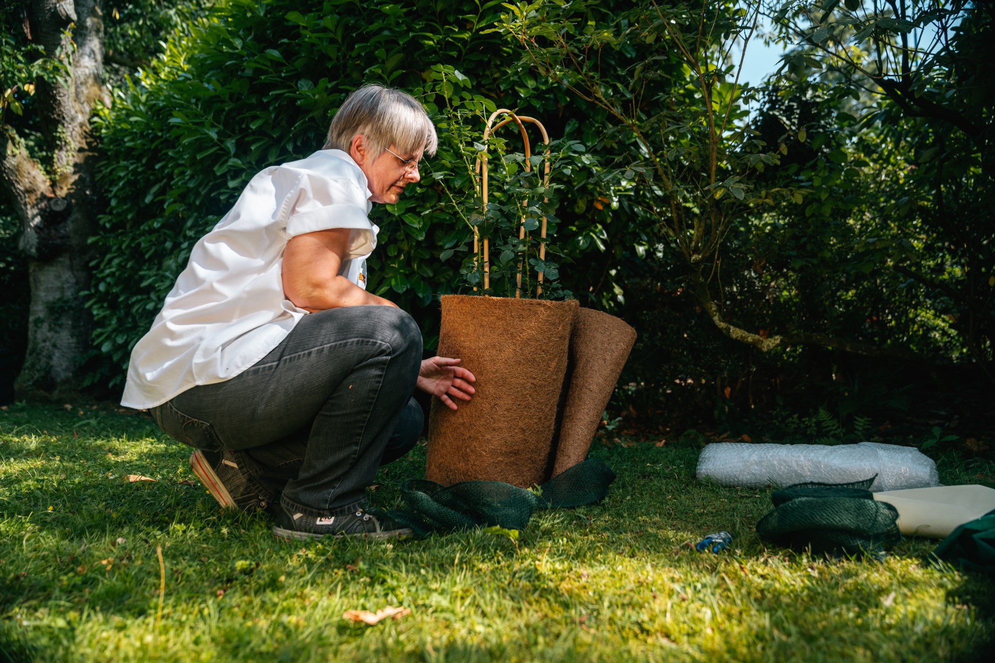 Nő a cserepes növény cserepét kókuszszőnyeggel csomagolja be az őszi kertben