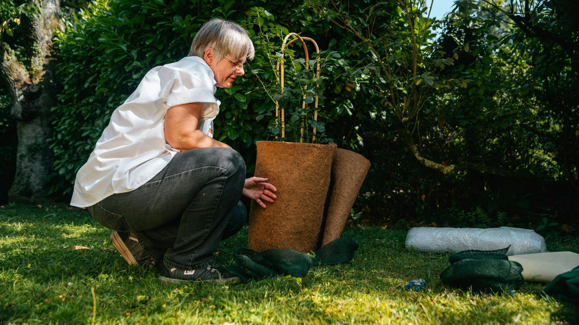 Nő a cserepes növény cserepét kókuszszőnyeggel csomagolja be az őszi kertben
