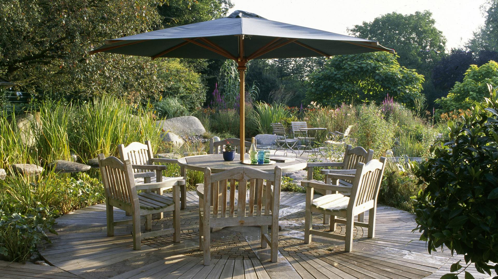 Große Holzterrasse mit Holzmöbeln und einem Sonnenschirm.