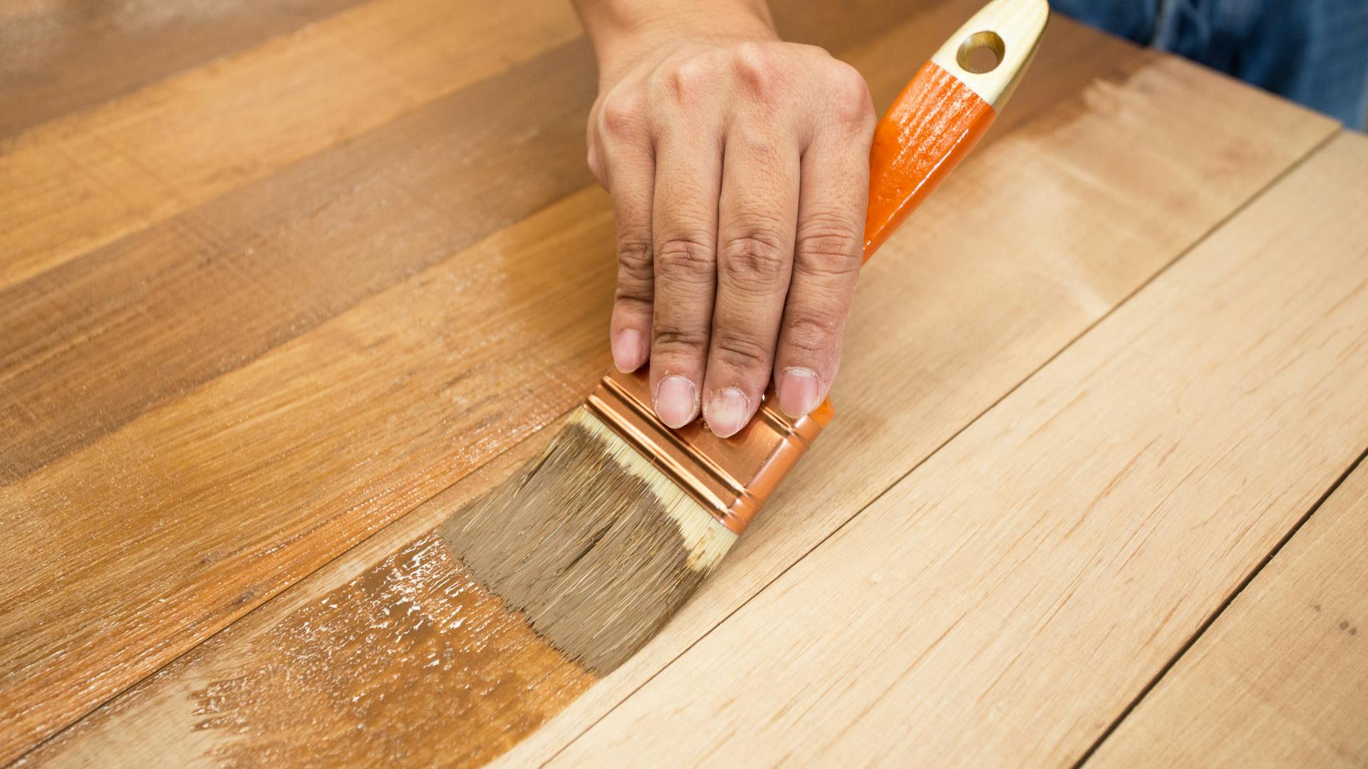 Jemand trägt Lasur mit einem Pinsel auf Holz auf.