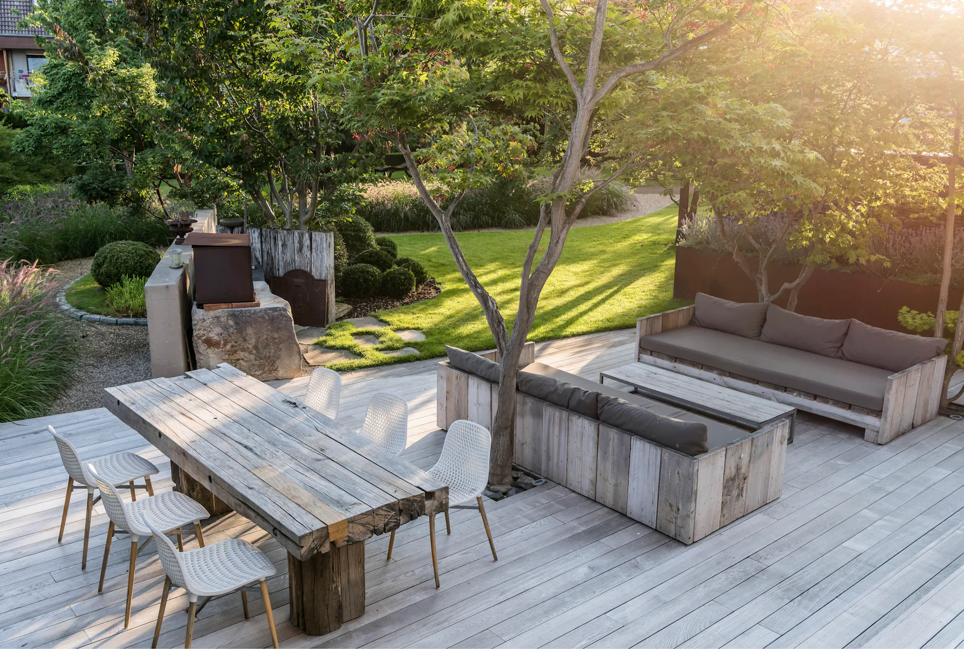 Holzterrasse mit Holzmöbeln in einem grossen grünen Garten.