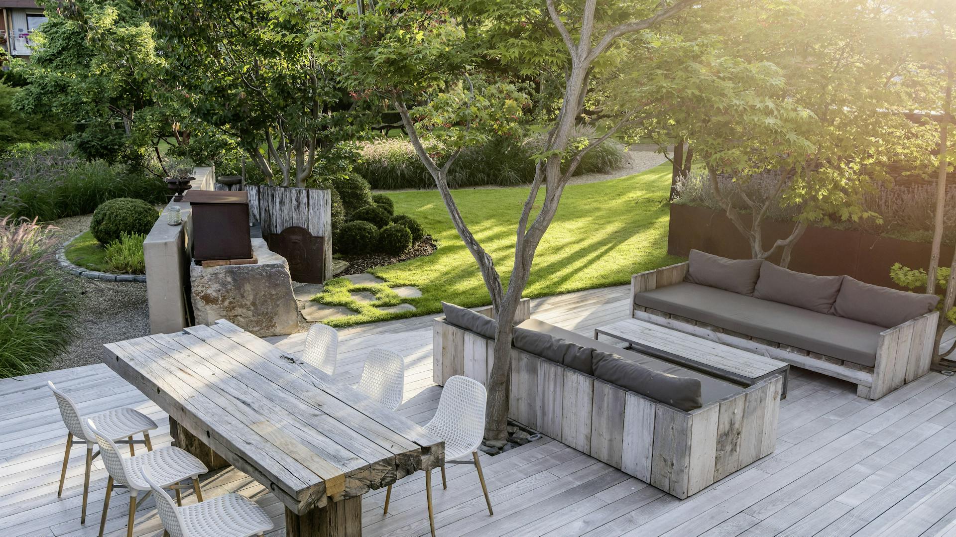 Holzterrasse mit Holzmöbeln in einem großen grünen Garten.