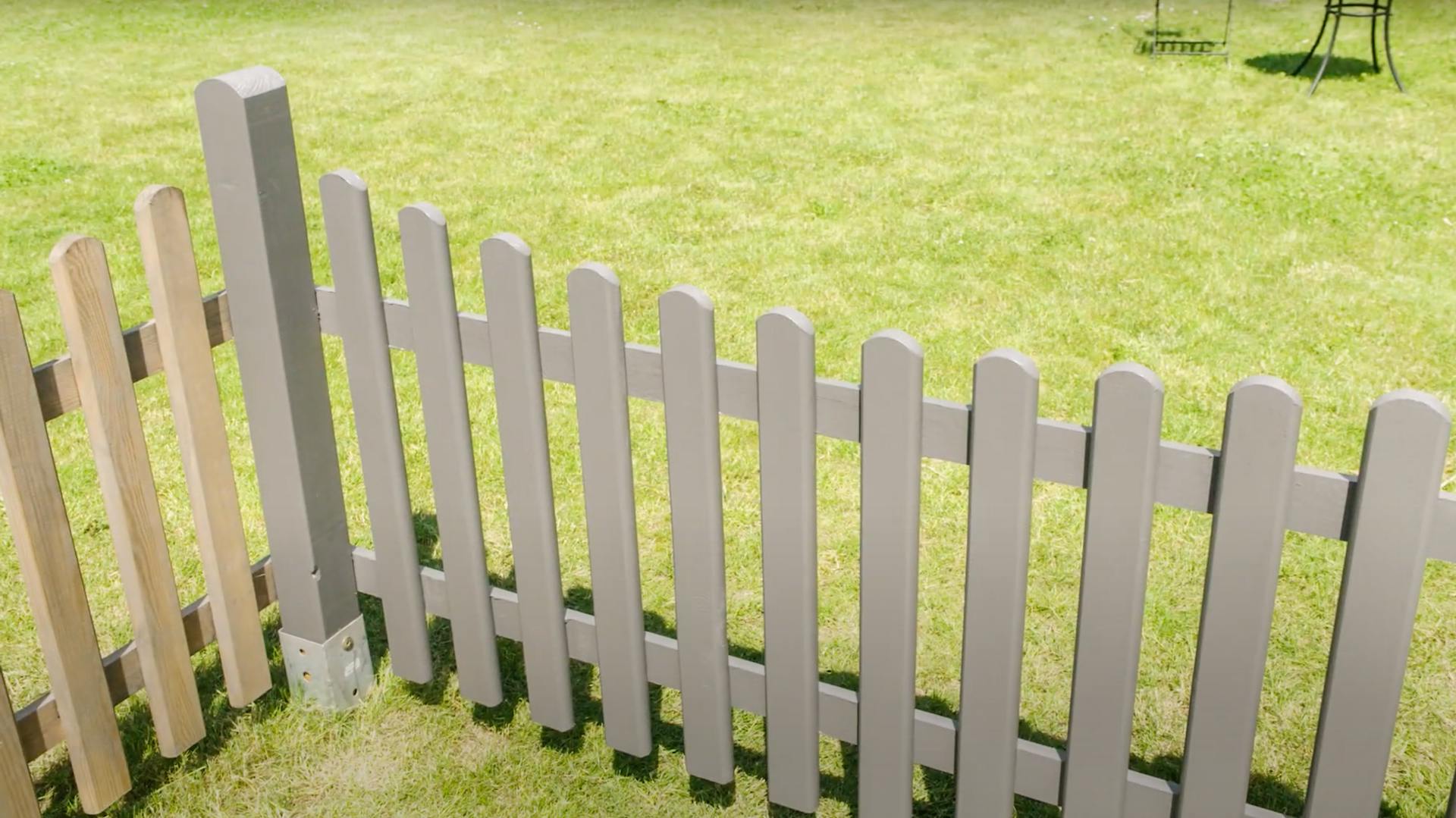 Ein fertig lackierter grauer Holzzaun auf einer Wiese.