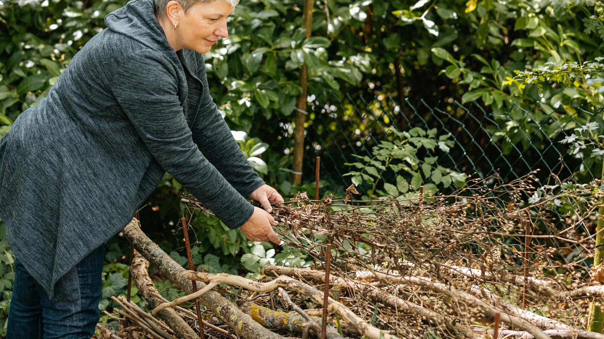 Frau legt Holz und Laub auf einen Holzstapel im Garten.