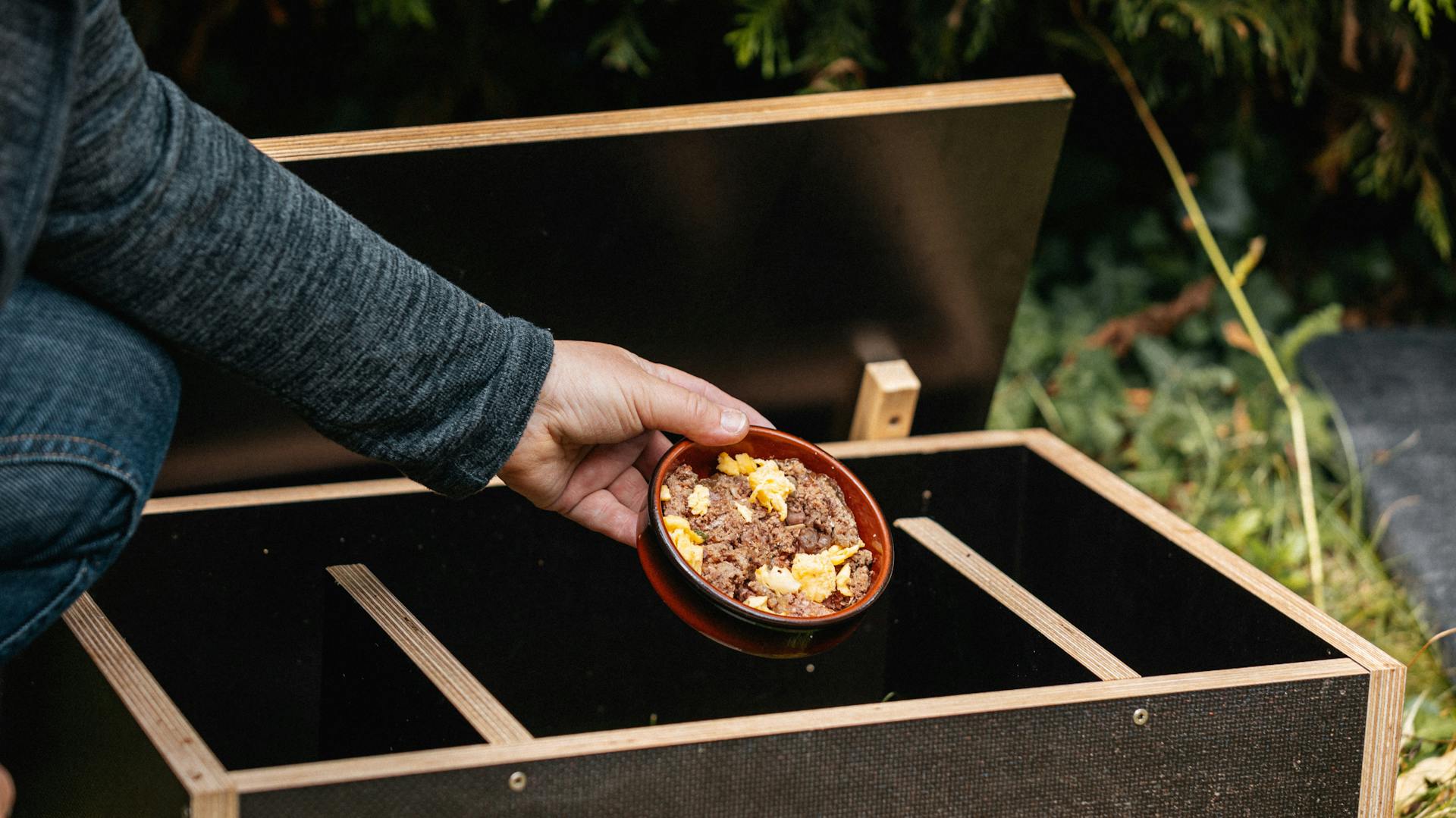 Eine Frau stellt einen Napf mit Faschiertem und Rührei in ein Igelhaus.