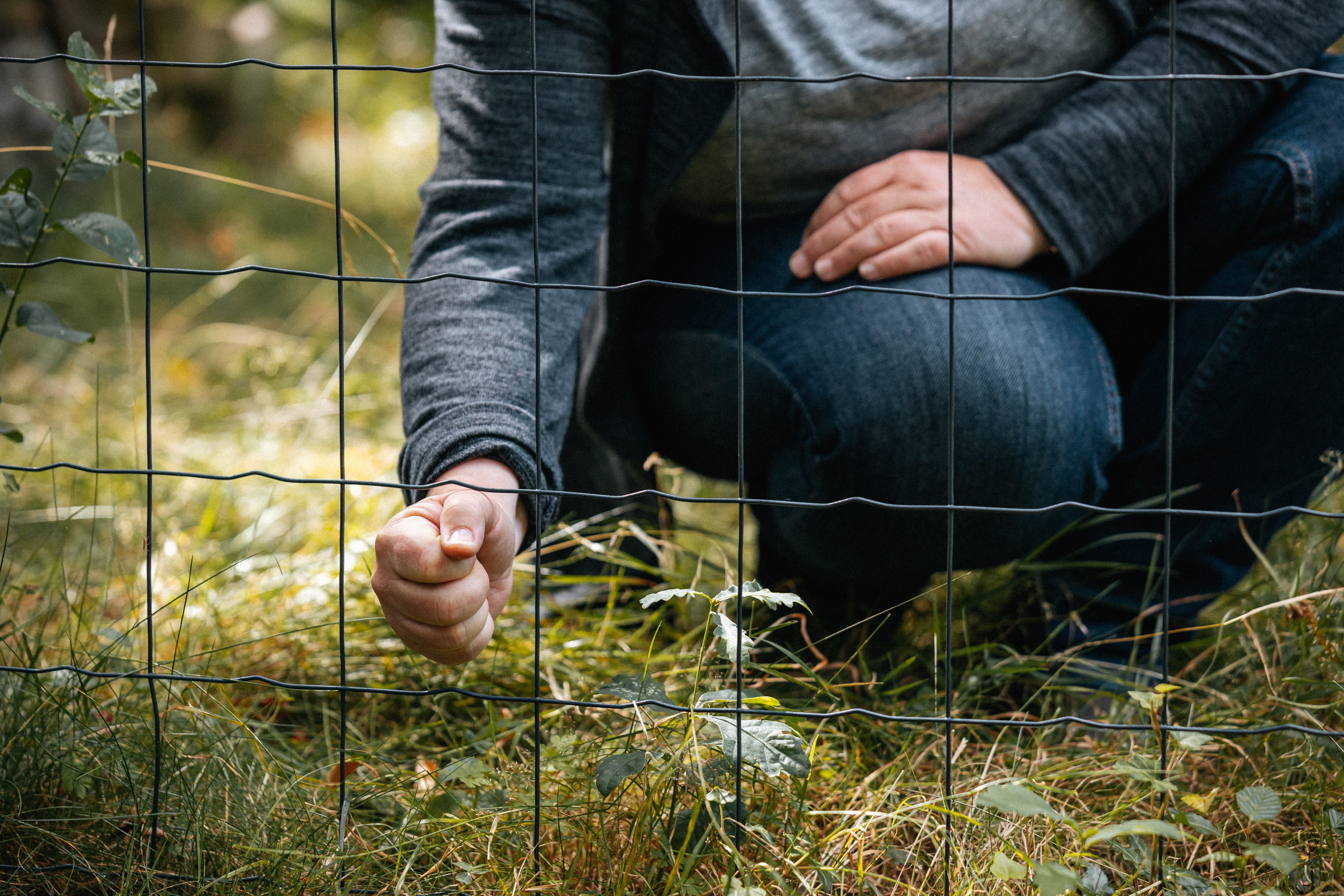 Frau steckt ihre Faust durch einen Drahtzaun mit großen Maschen.