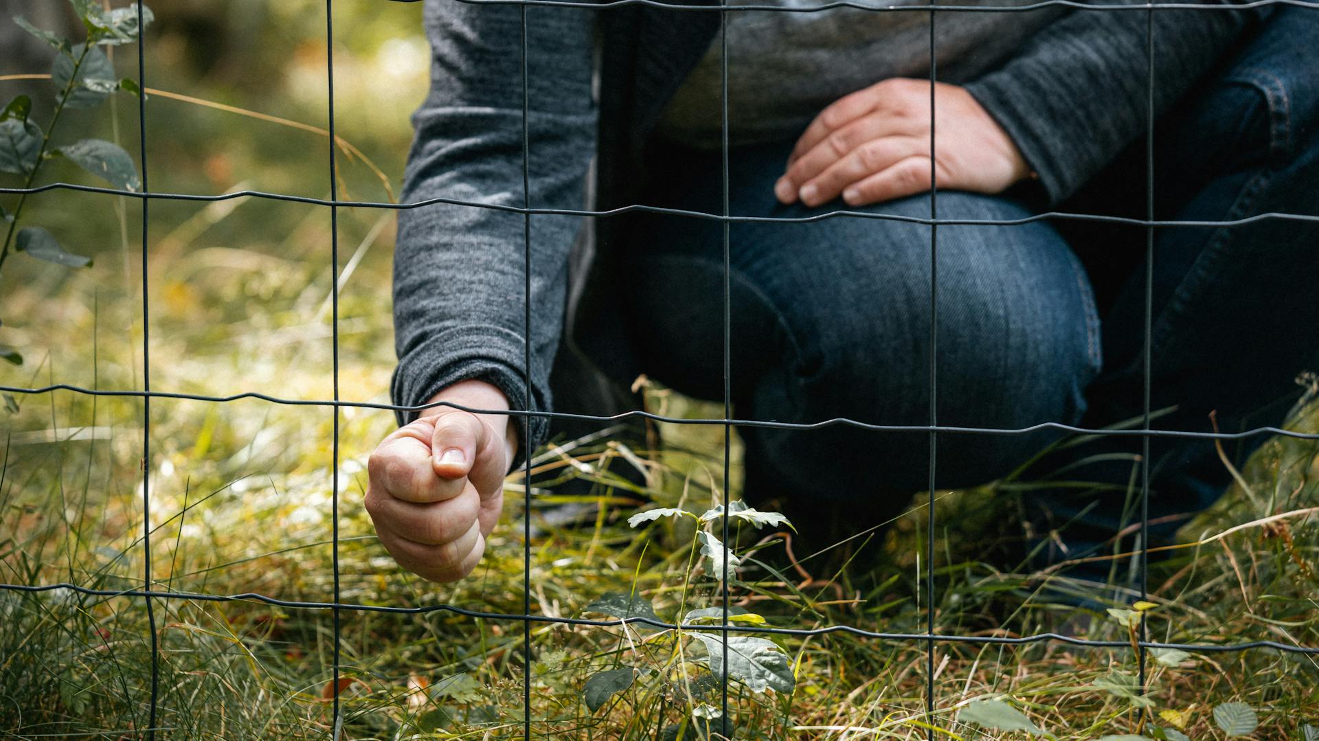 Frau steckt ihre Faust durch einen Drahtzaun mit großen Maschen.