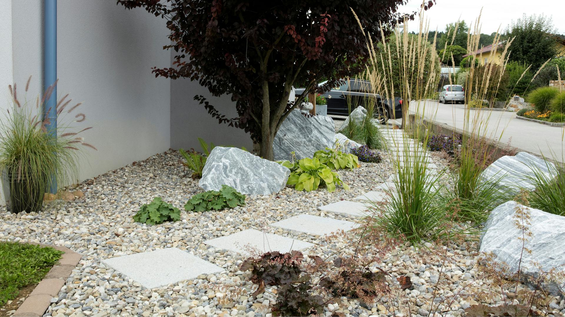 Nagy, világos és változatosan beültetett kavicsos kert egy háznál