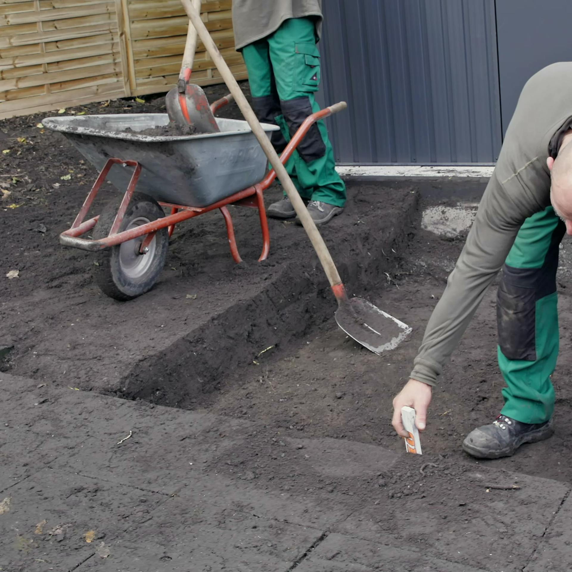 Heimwerker misst Tiefe des ausgehobenen Bodens für Kiesweg.