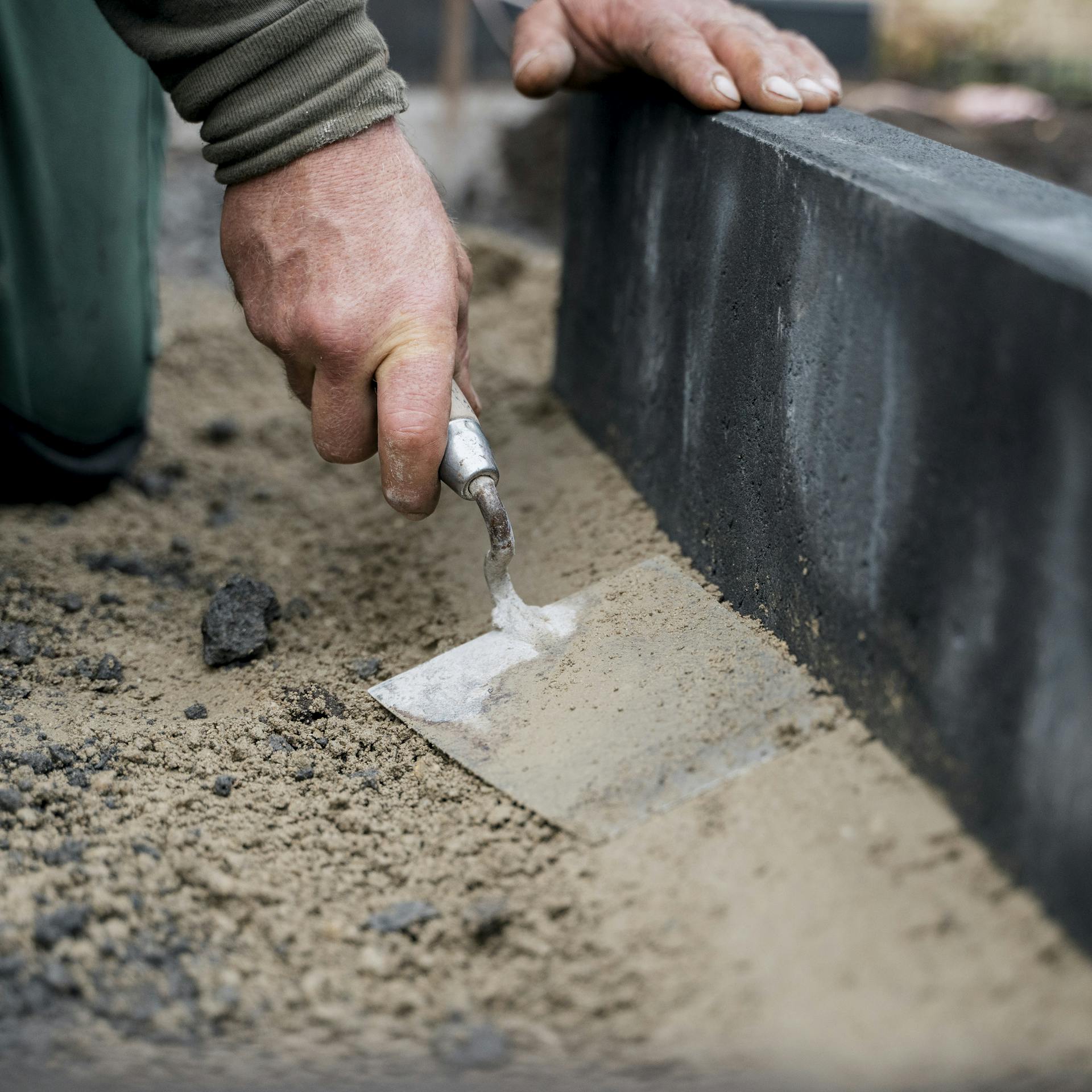 Eine Person formt eine Estrichstütze für einen Kantstein mit einer Maurerkelle