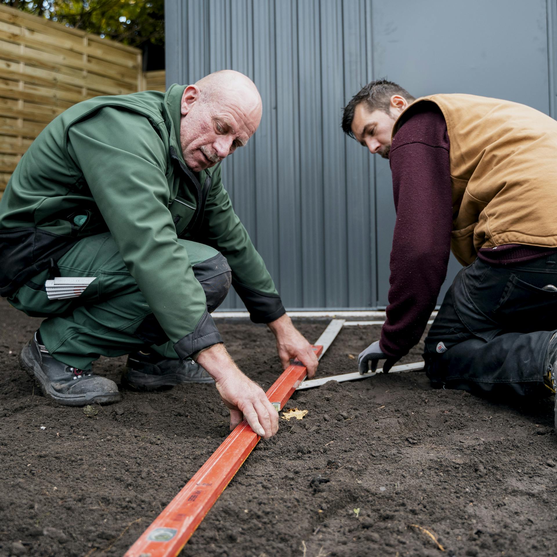 Heimwerker messen Verlauf für Gartenweg auf Boden im Garten mit Bauwinkel und Messlatte ab.