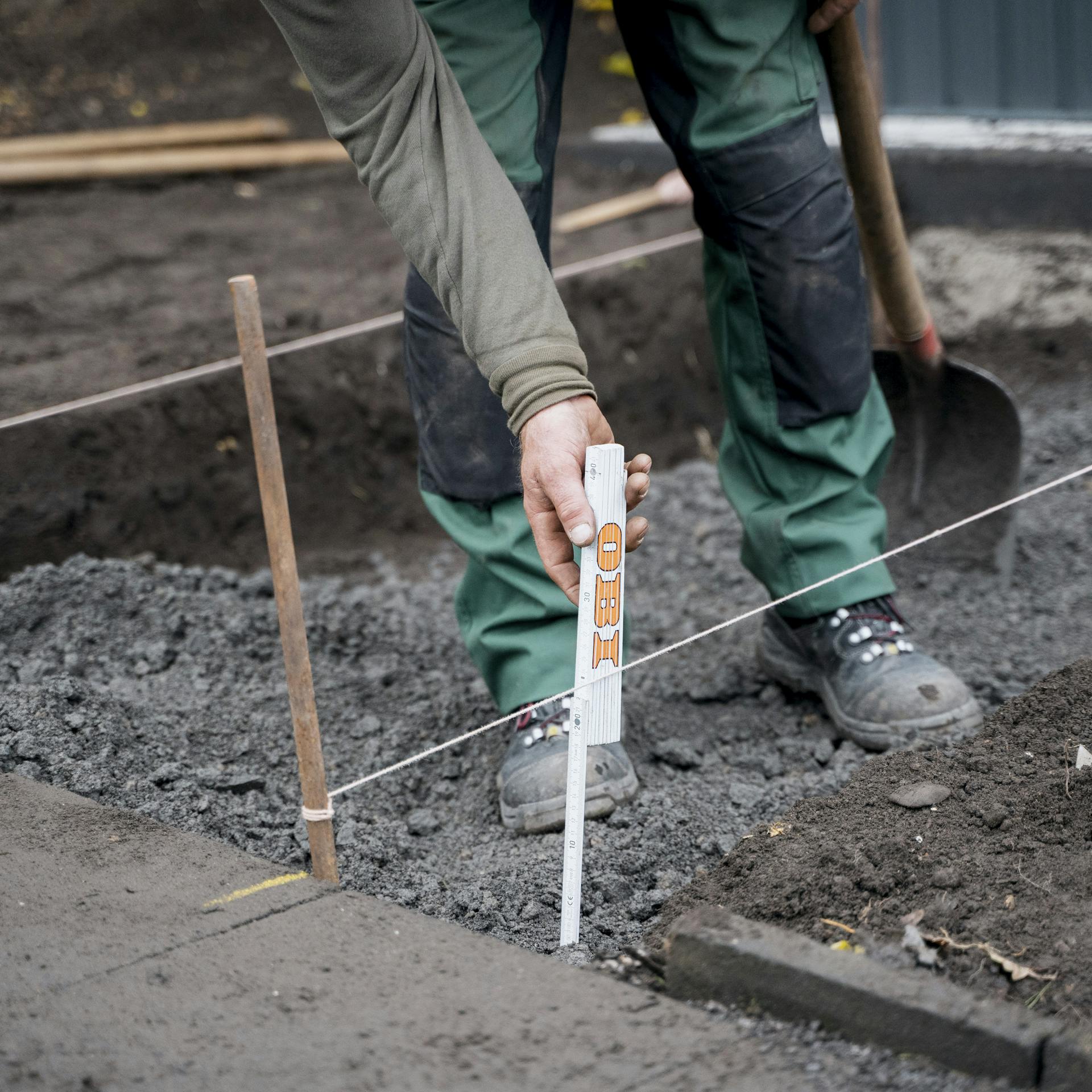 Eine Person misst die Höhe der Schotterschicht mit einem Zollstock