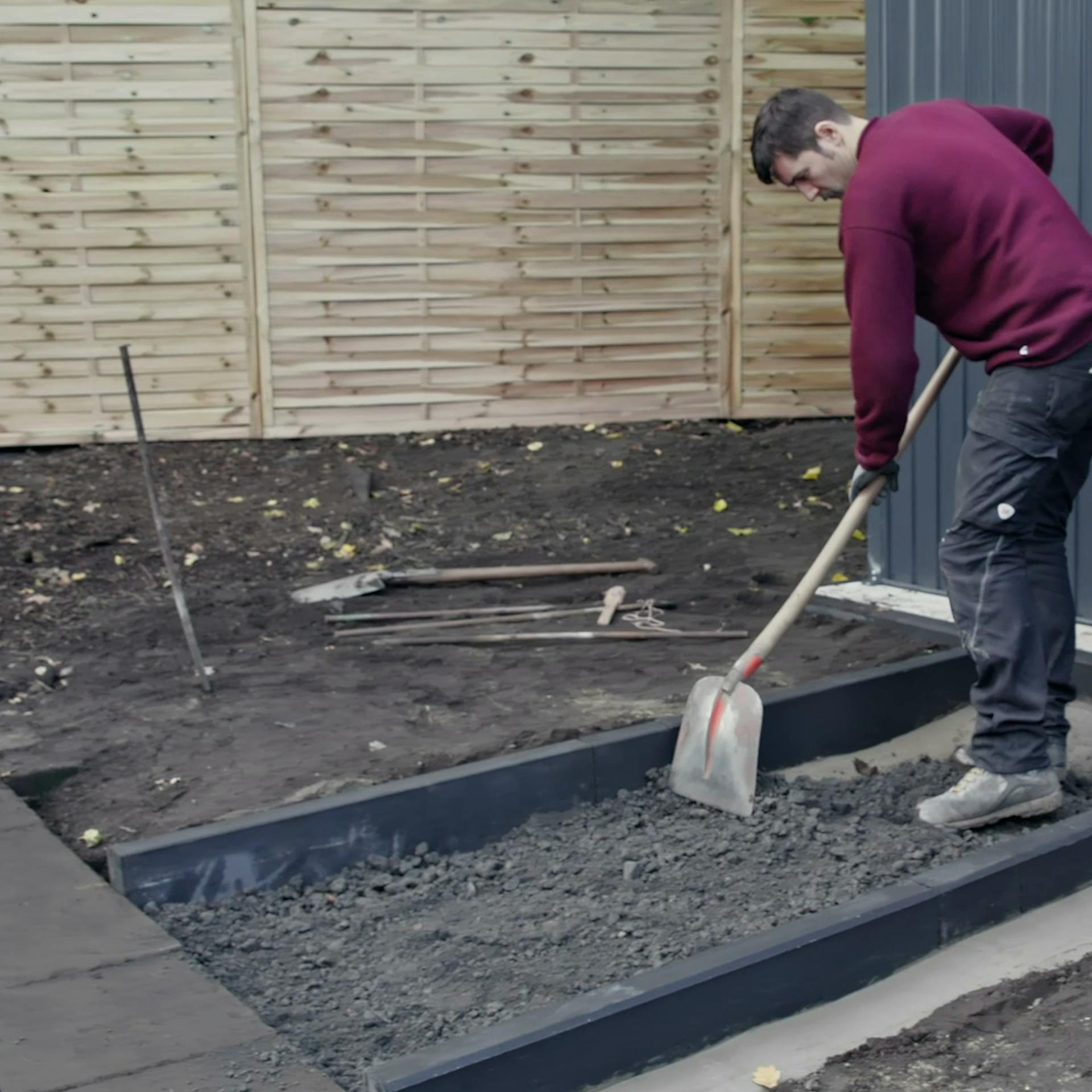 Heimwerker verteilen eingefüllten Schotter in ausgehobenem Graben mit der Schaufel.