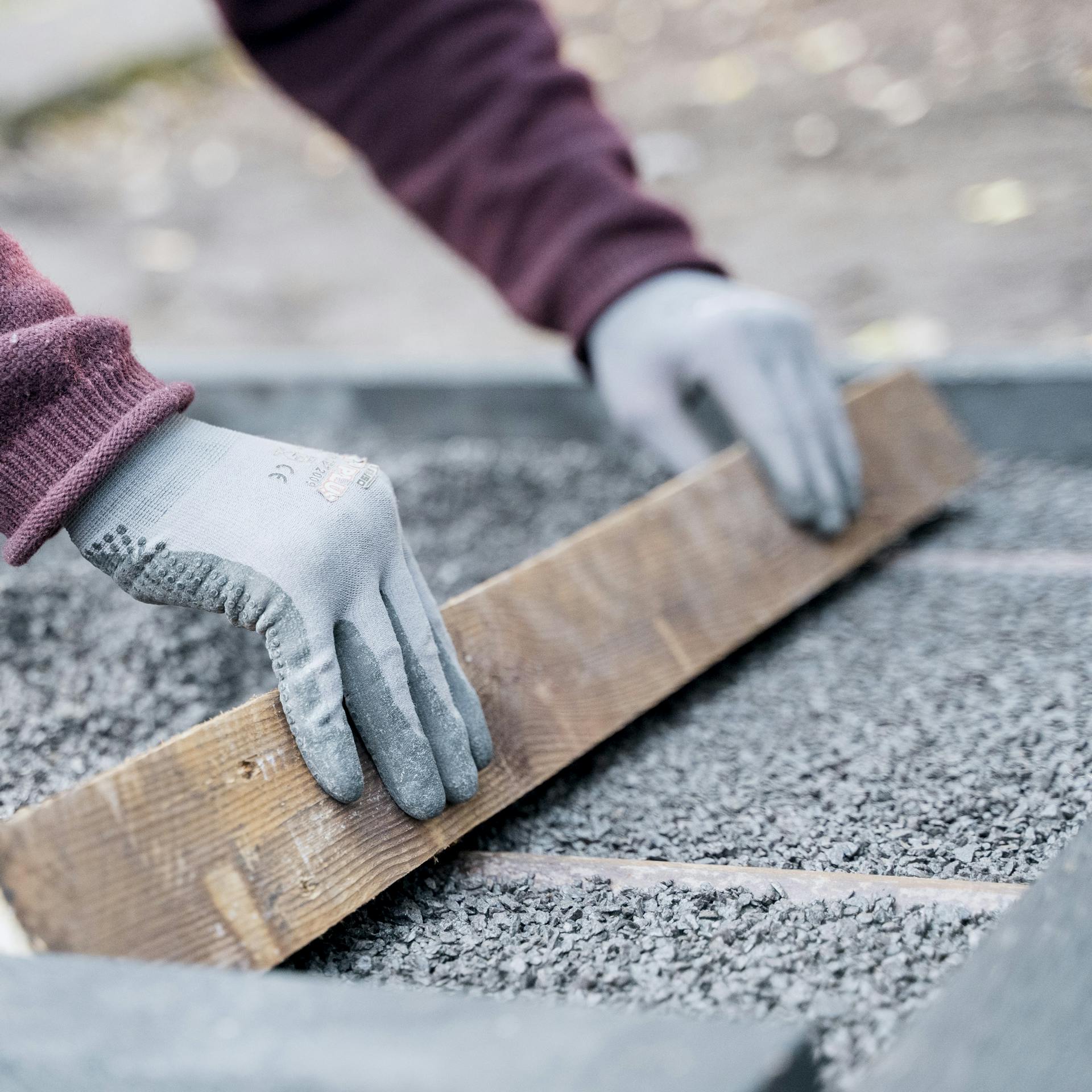 Heimwerker zieht Splitt mit einem Kantholz über Abziehrohr ab, um Ausgleichsschicht zu nivellieren.