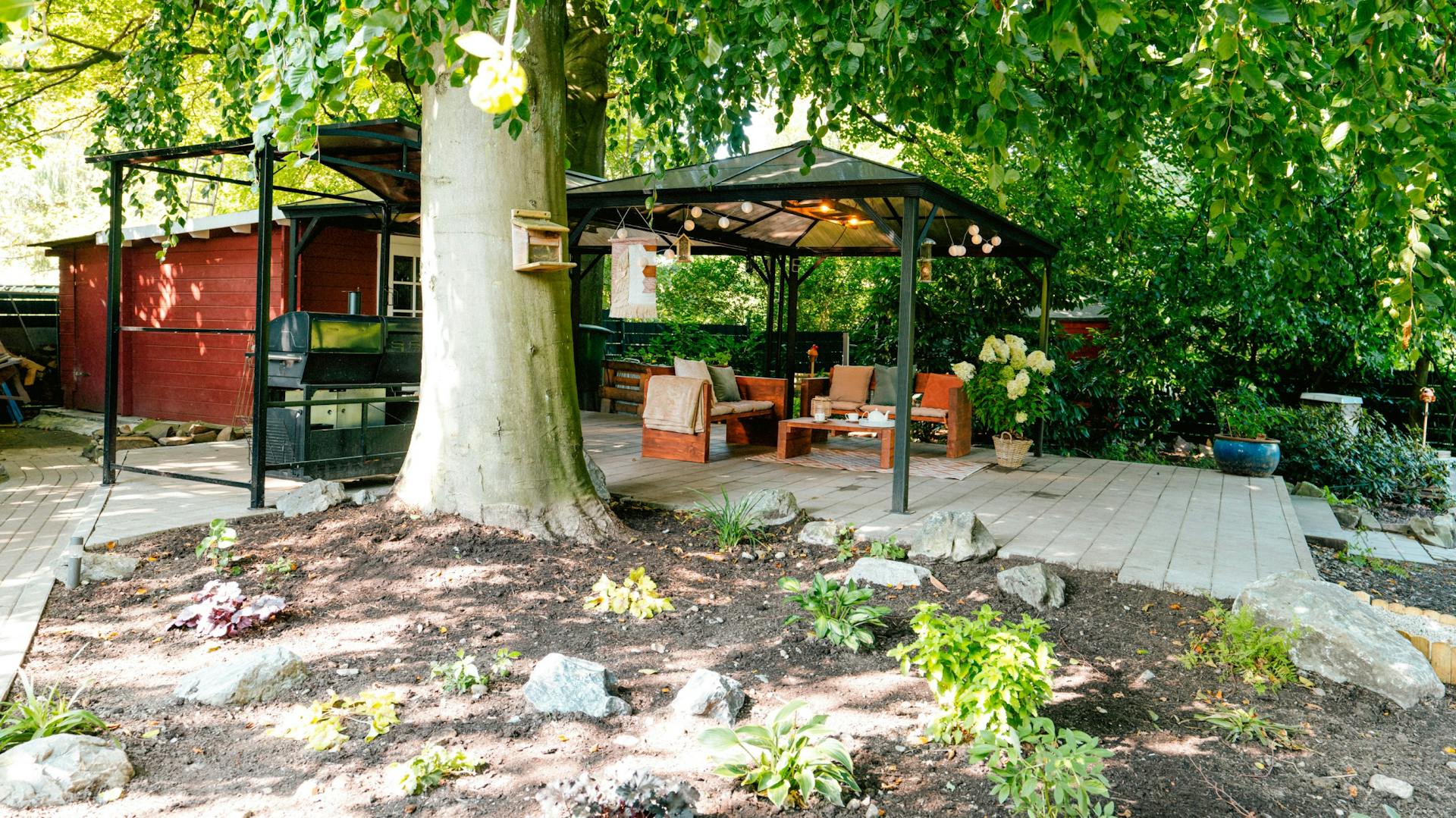 Pavillon mit Sitzgruppe hinter einem Baum