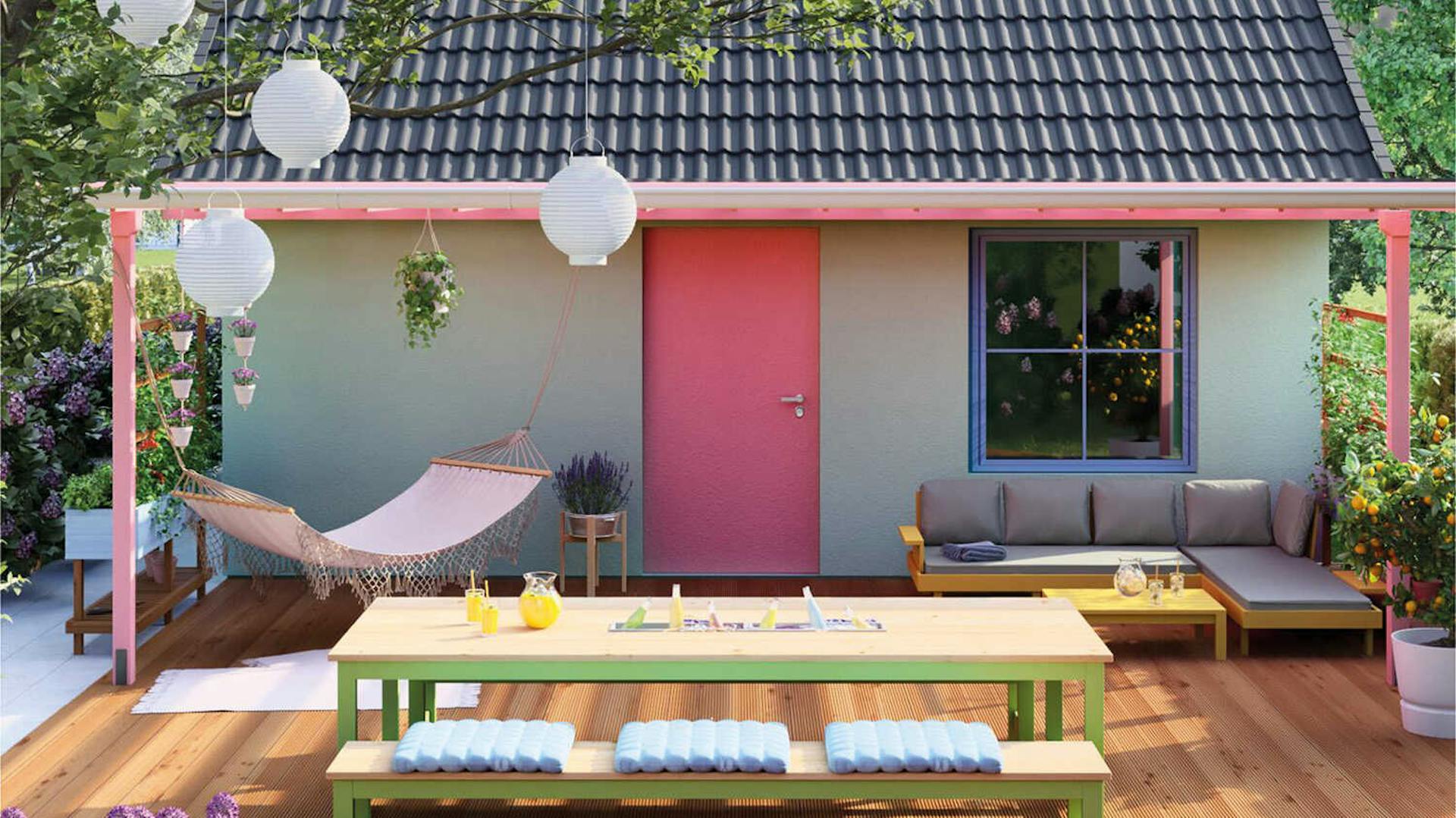 Vor einem kleinen Häuschen steht unter dem Fenster ein Sofa. An einer Überdachung wurde eine Hängematte befestigt. Davor steht ein Tisch mit einer Bank.