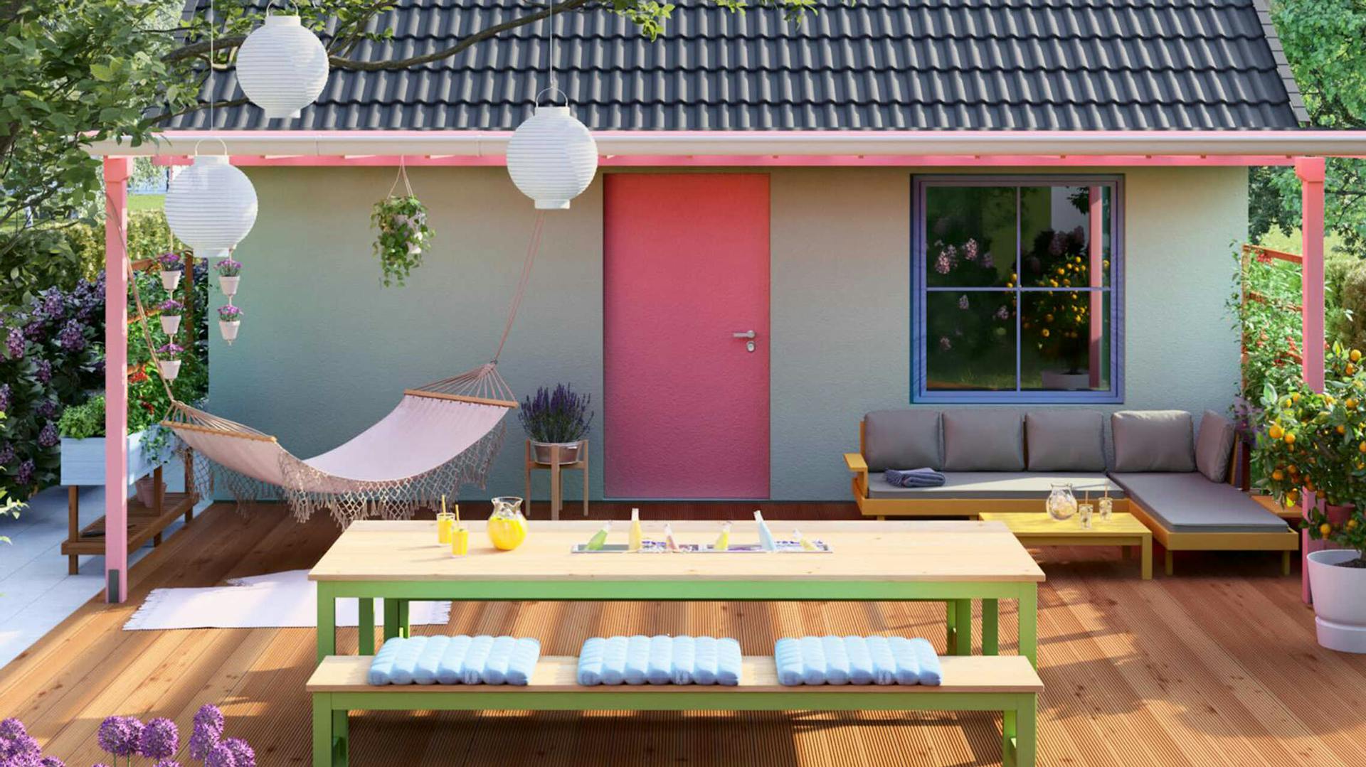 Vor einem kleinen Häuschen steht unter dem Fenster ein Sofa. An einer Überdachung wurde eine Hängematte befestigt. Davor steht ein Tisch mit einer Bank.