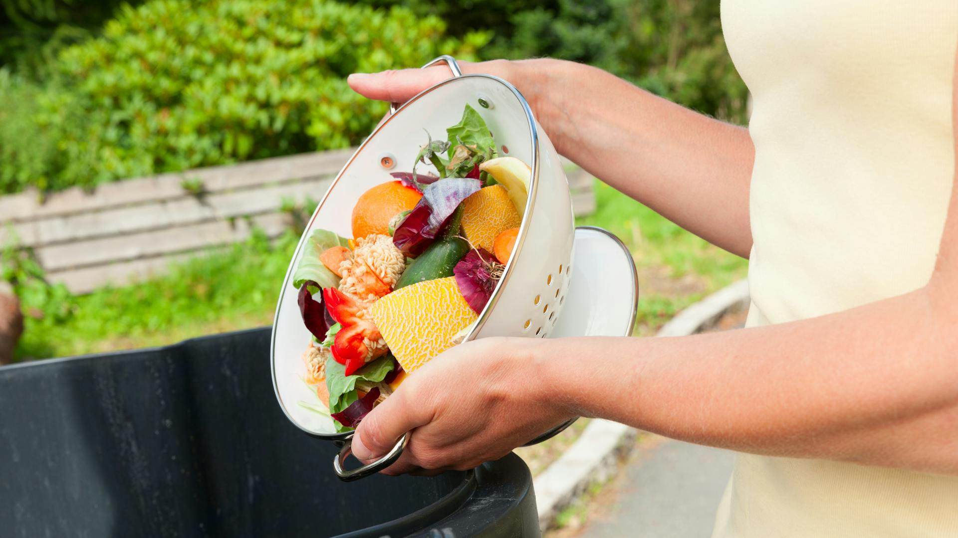 Jemand entsorgt Küchenabfälle in der Biotonne.