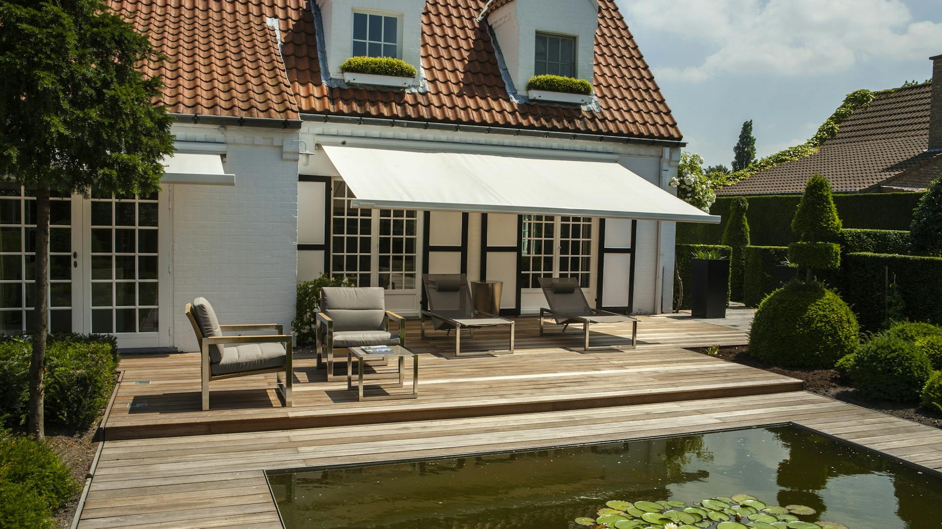 Sitzbereich auf Holzterrasse beschattet durch eine Gelenkmarkise an der Hauswand