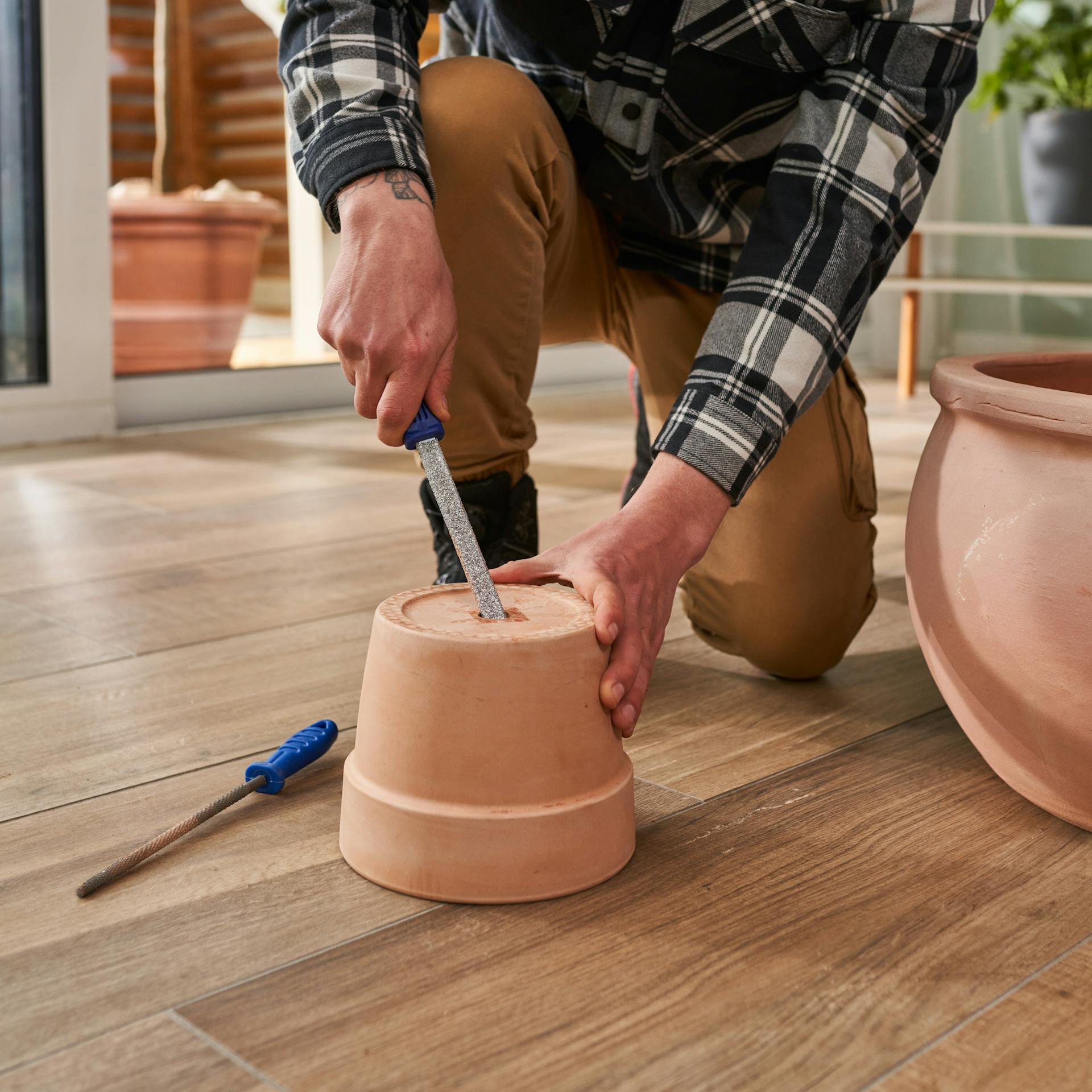 Mann vergrößert mit einer Feile die Öffnung eines Pflanztopfs.