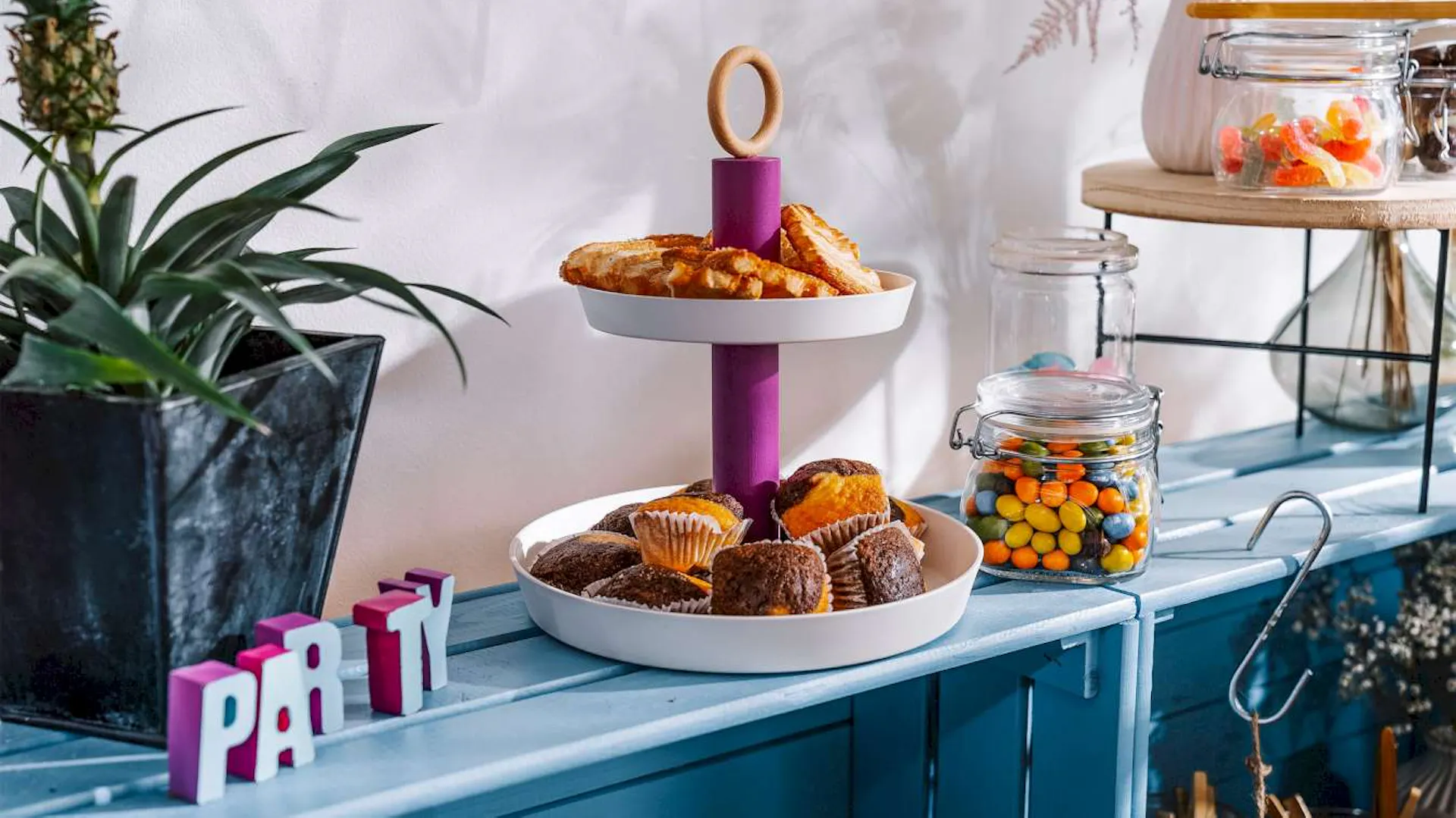 Eine DIY-Etagere steht auf einem hellblauen Regal neben einer Pflanze und Süßigkeiten in Drahtbügelgläsern.