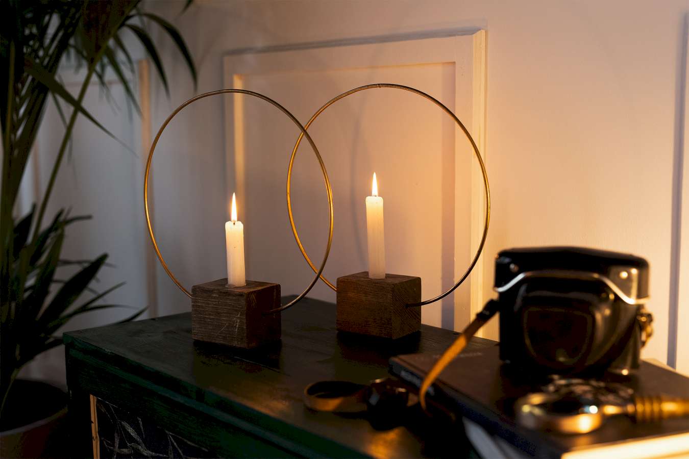Zwei Kerzenständer aus Holzwürfeln und Messingringen stehen auf einem regal neben einer Kamera.
