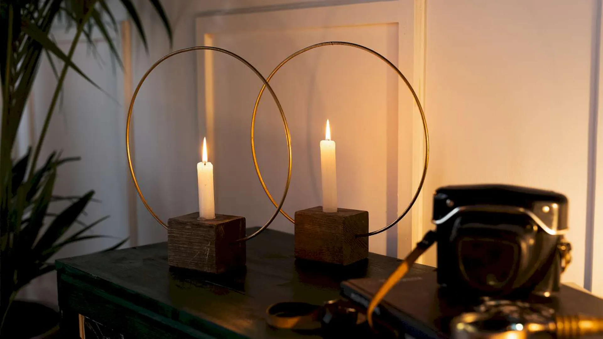 Zwei Kerzenständer aus Holzwürfeln und Messingringen stehen auf einem regal neben einer Kamera.