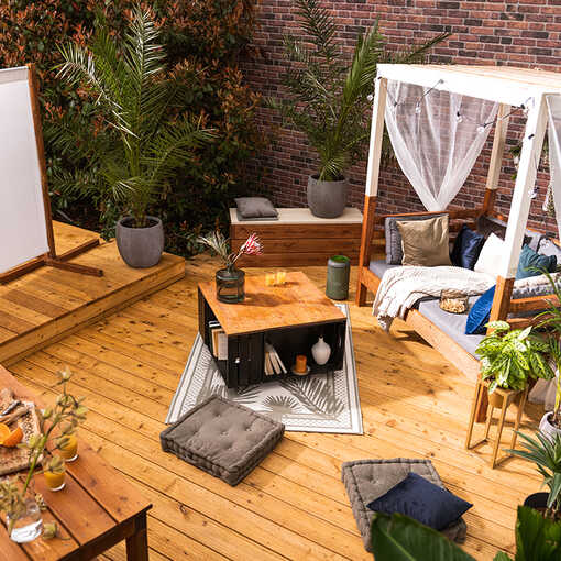 Eine Terrasse auf der eine Leinwand vor die Sonneninsel Helena platziert wurde und zwischen den beiden eine Bank Alfred und ein Couchtisch Vierfach stehen.
