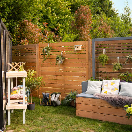 Das Hochbeet Alfred steht an einer Gartenwand, wo Hängetöpfe und ein Vogelhaus angebracht worden sind.