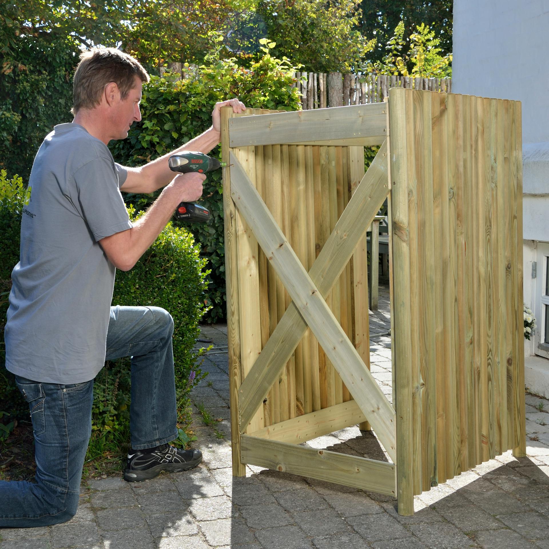 Osoba skrutkuje priečne laty na zadnú stranu boxu na smetnú nádobu