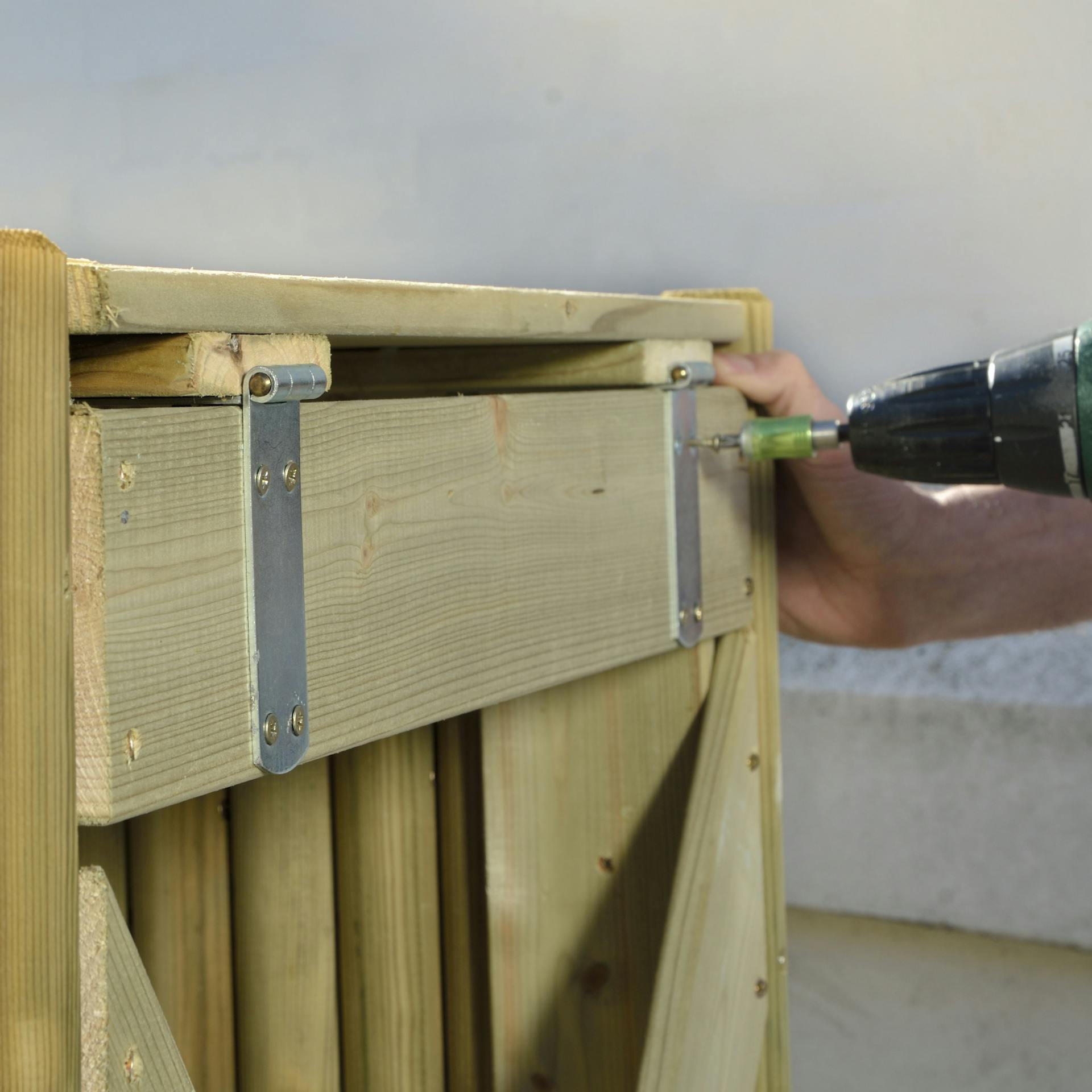 Osoba skrutkuje závesy na box na smetnú nádobu