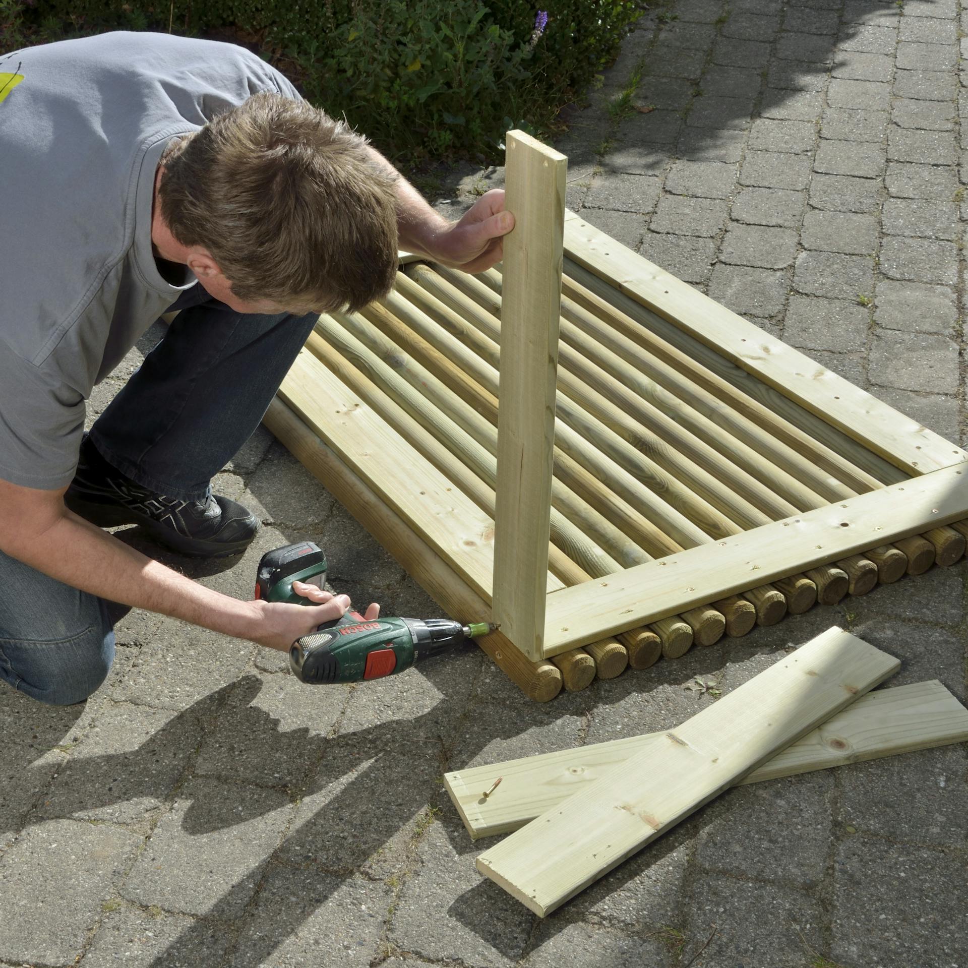 Osoba skrutkuje priečne laty na box na smetnú nádobu