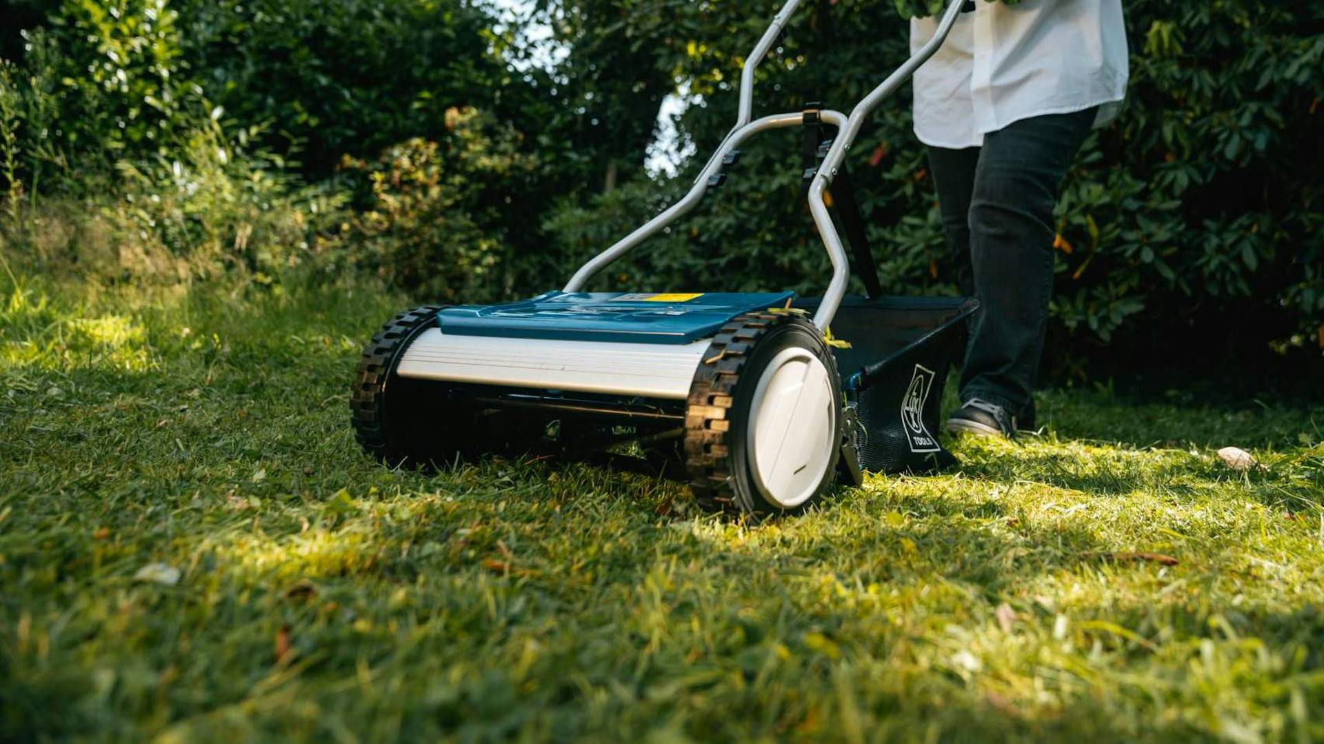 Mensch mäht mit manuellem Rasenmäher den Rasen