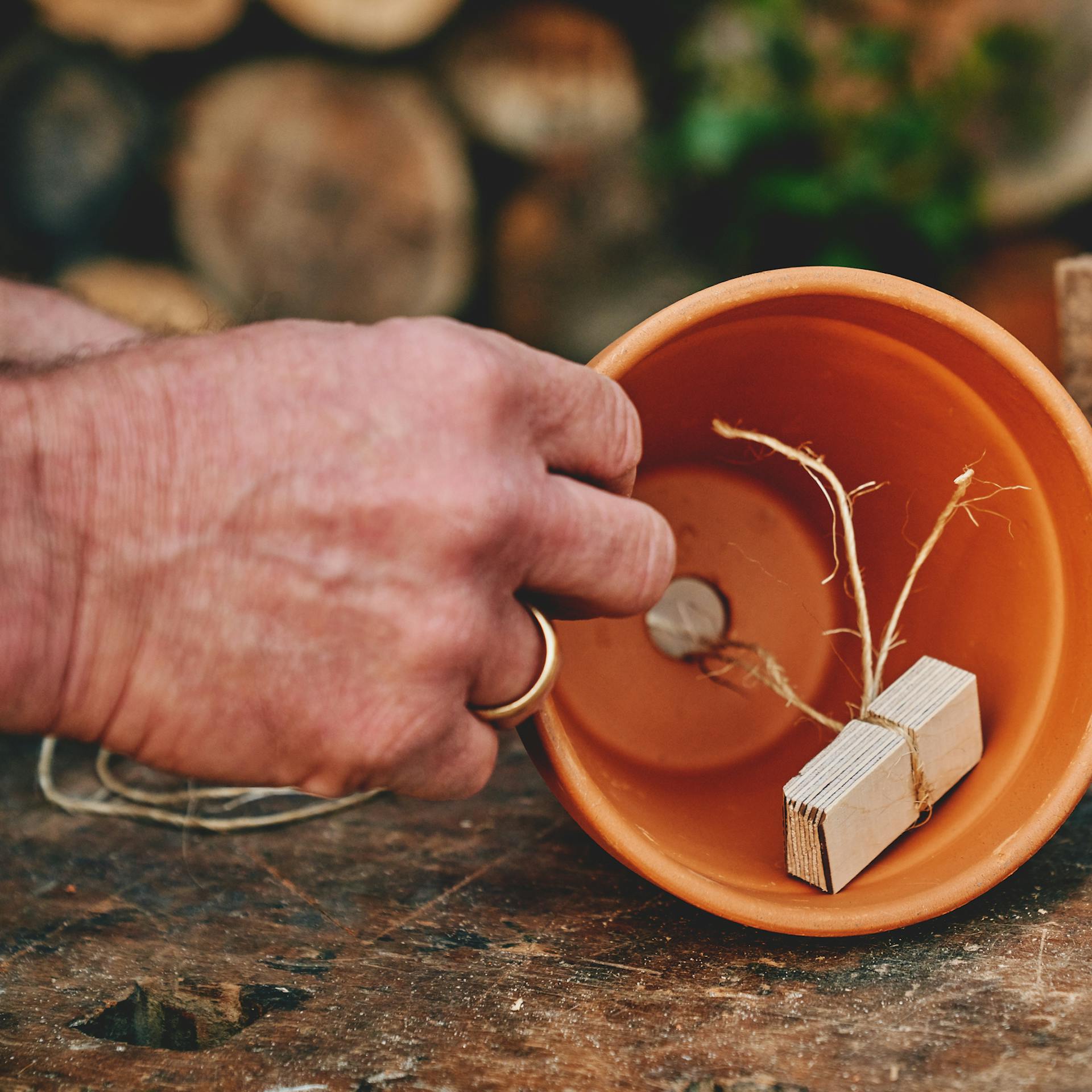 Person befestigt Schnur mit Holzstück in Tontopf.