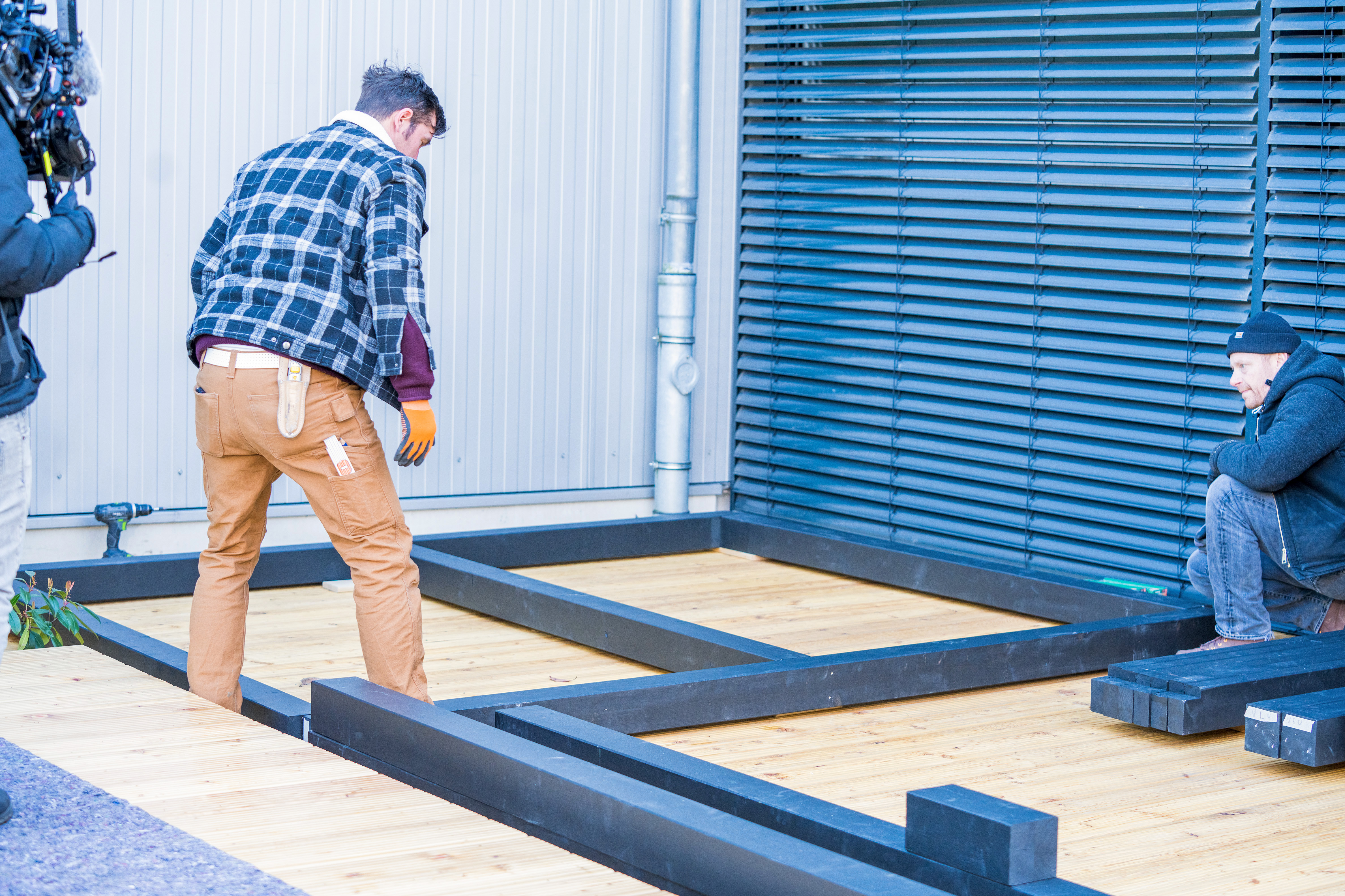 Zwei Heimwerker legen die Balken der Gartenlaube auf einer Terrasse zurecht