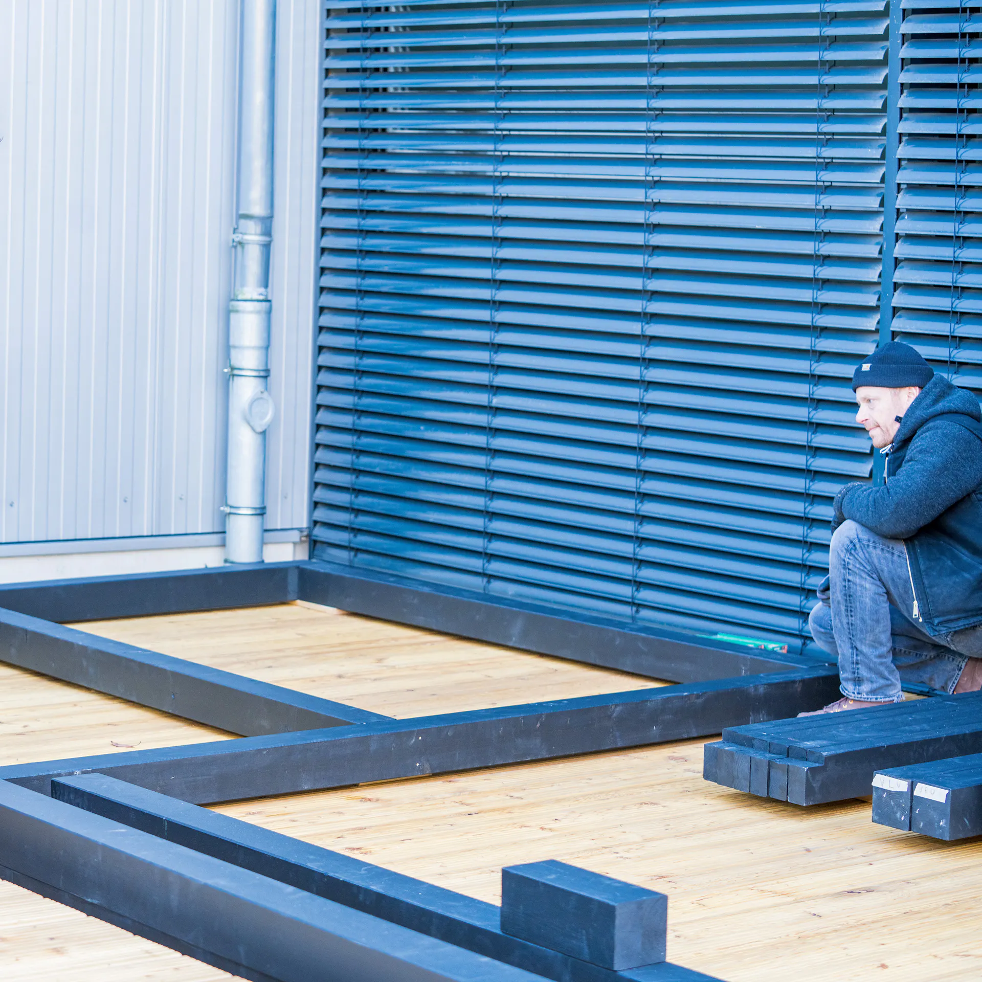 Zwei Heimwerker legen die Balken der Gartenlaube auf einer Terrasse zurecht
