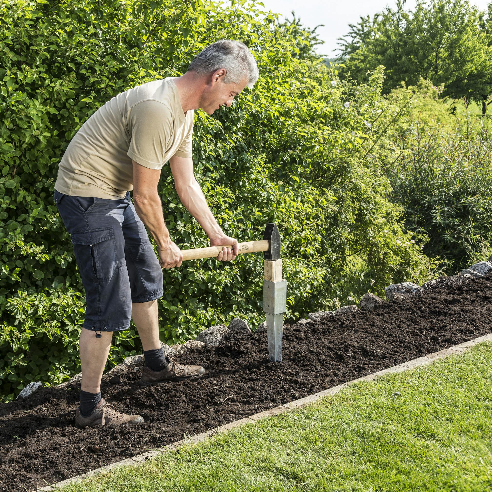 Mann schlägt mit Vorschlaghammer Einschlaghülsen in die Erde