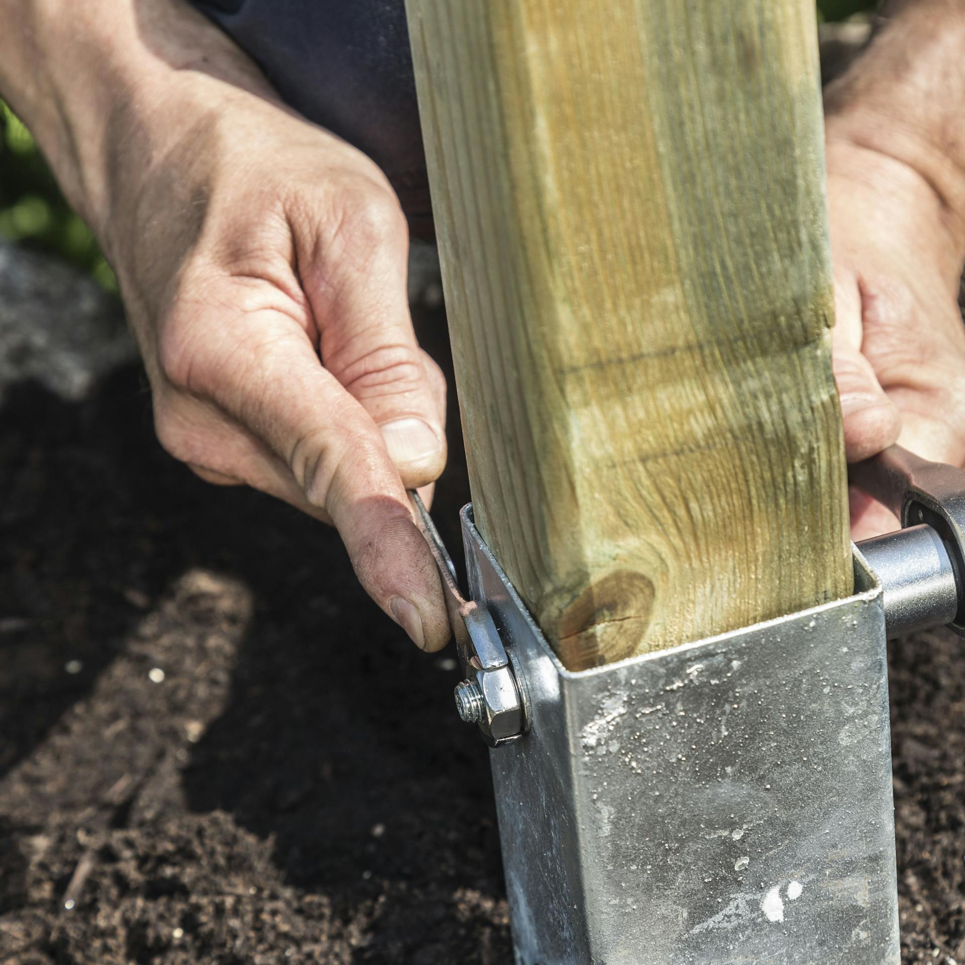 Jemand verschraubt einen Holzpfosten in einer Bodeneinschlaghülse
