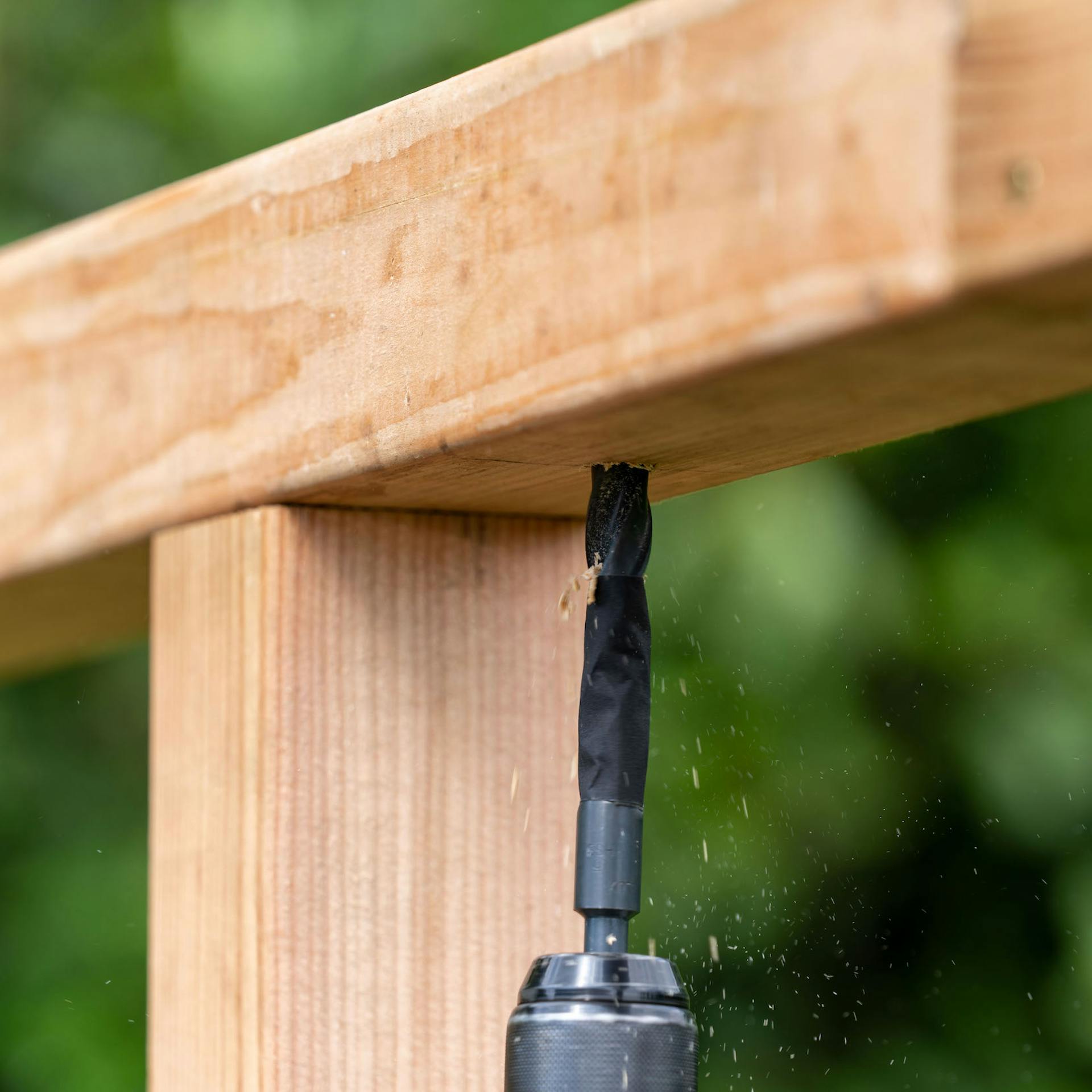 Egy személy lyukakat fúr egy négyzet alakú fába.