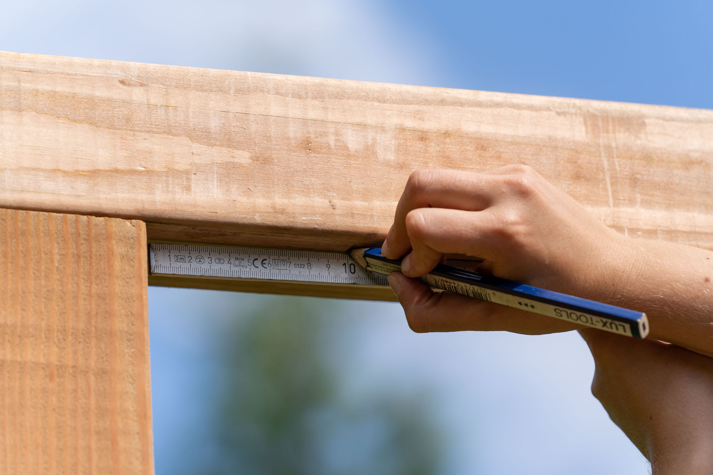 A személy ceruzával pontokat rajzol egy négyzet alakú fadarabra.