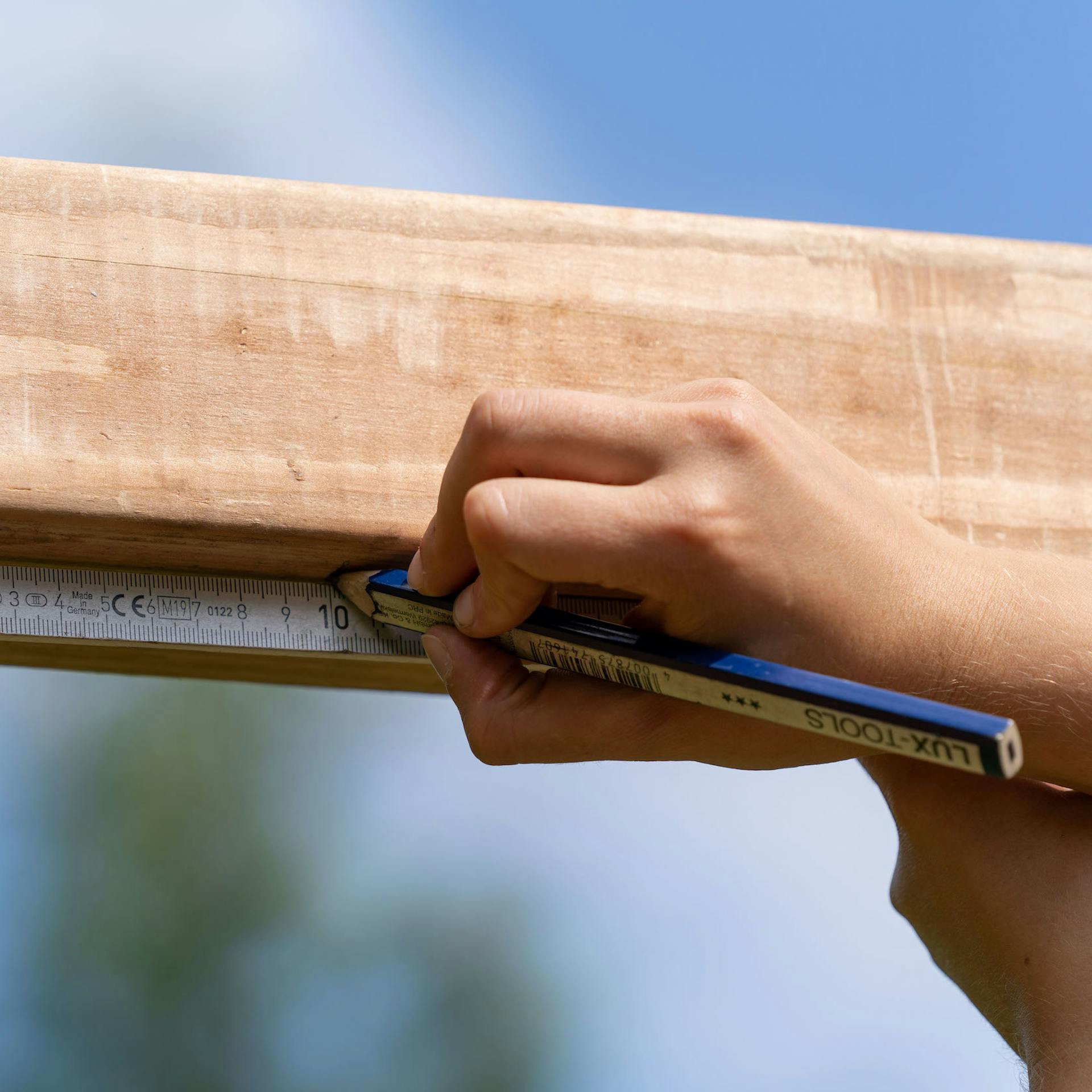 A személy ceruzával pontokat rajzol egy négyzet alakú fadarabra.