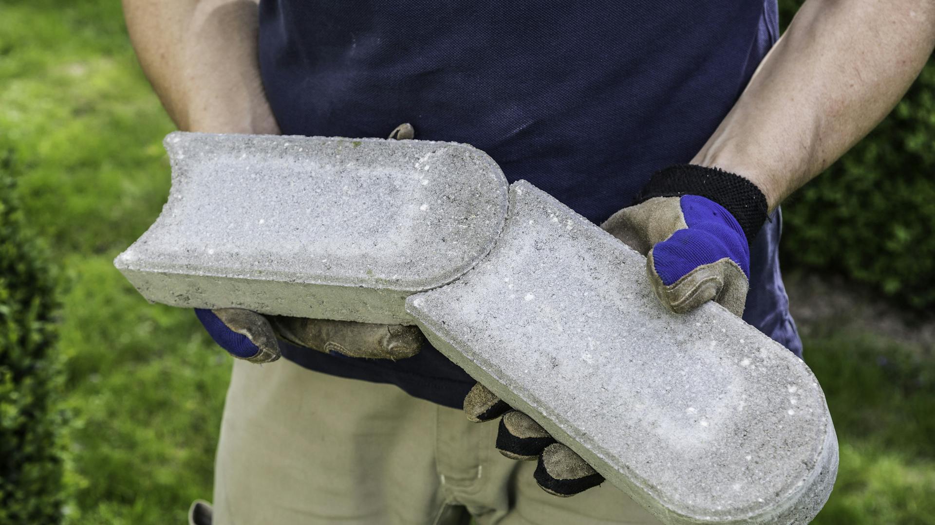 Eine Person hält zwei Rasenkantensteine in Schwalbenschwanzform in den Händen