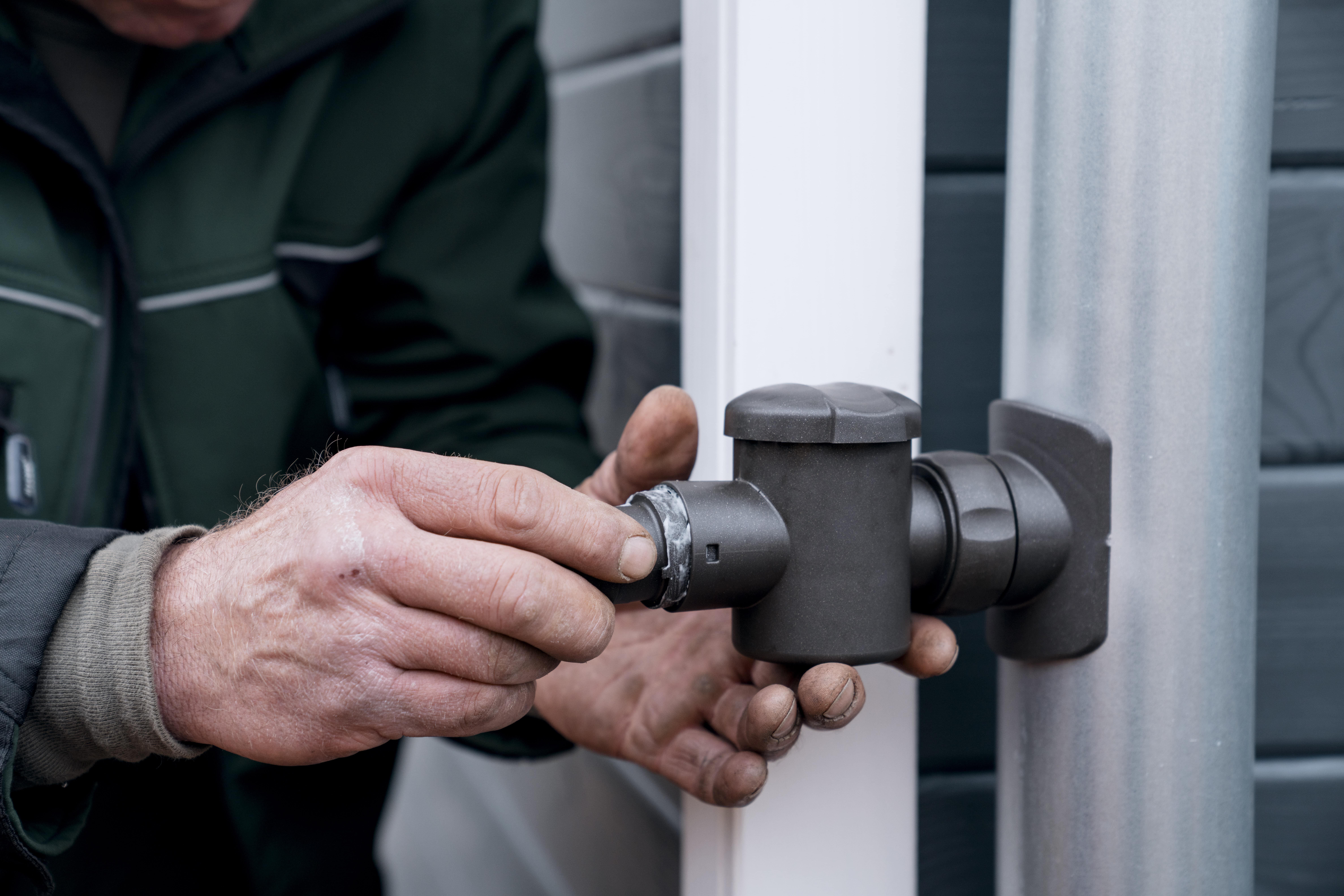 ein Handwerker montiert den Regensammler am Fallrohr.