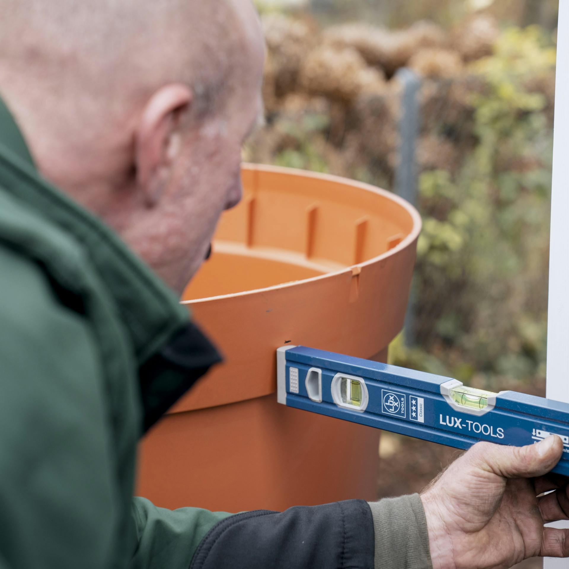 Ein Handwerker prüft Höhe und Position für die Verbindung von Fallrohr und Regentonne mit einer Wasserwaage.