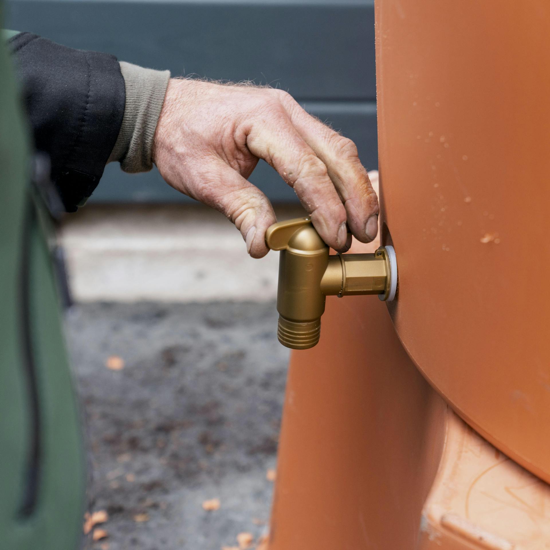 Handwerker montiert Wasserhahn an einer Regentonne.