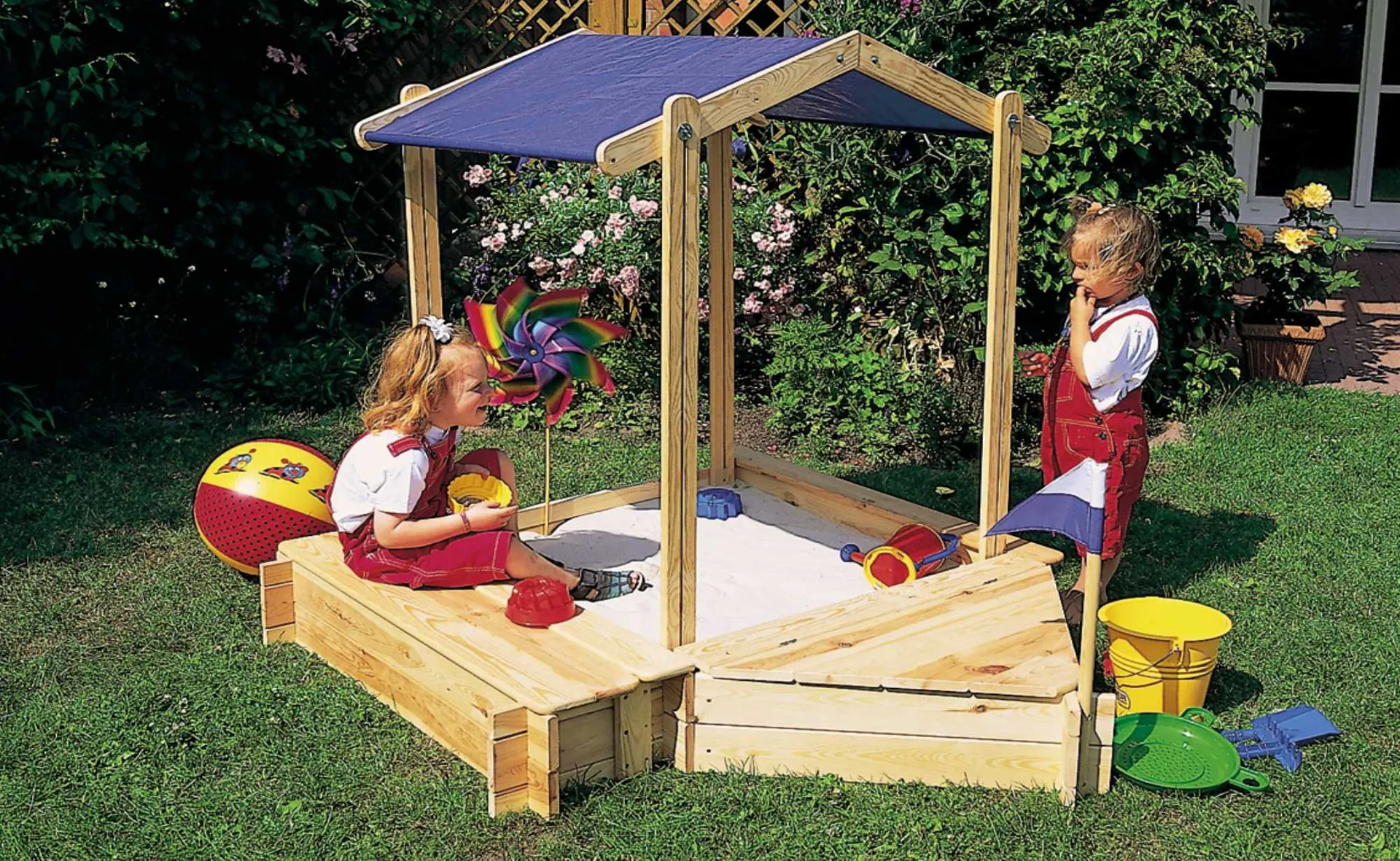 Due bambini giocano in una sabbiera con tetto blu.
