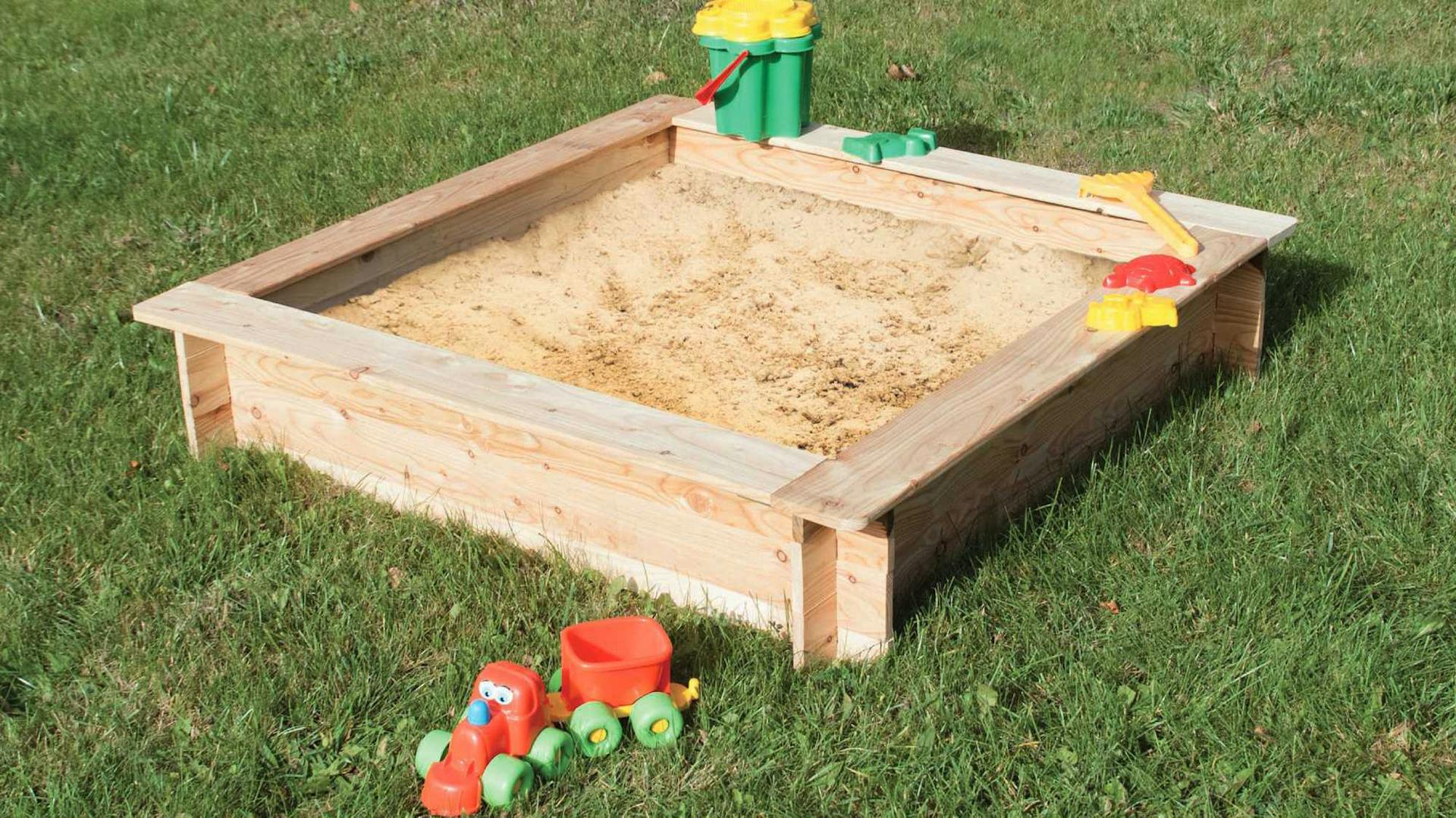 Holz-Sandkasten mit Sand gefüllt und mit Sandspielzeug steht auf grünem Rasen.