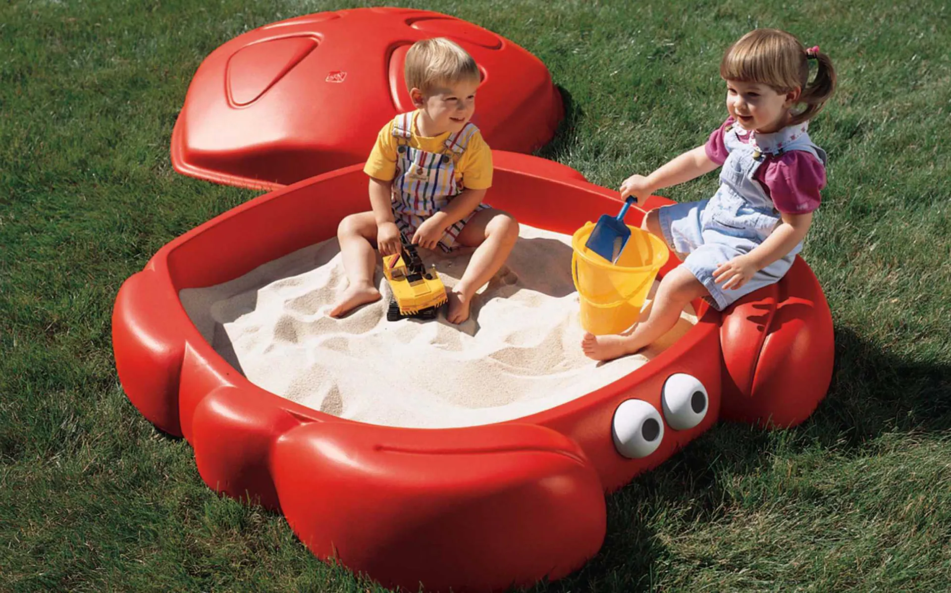 Due bambini giocano in una sabbiera di plastica rossa.